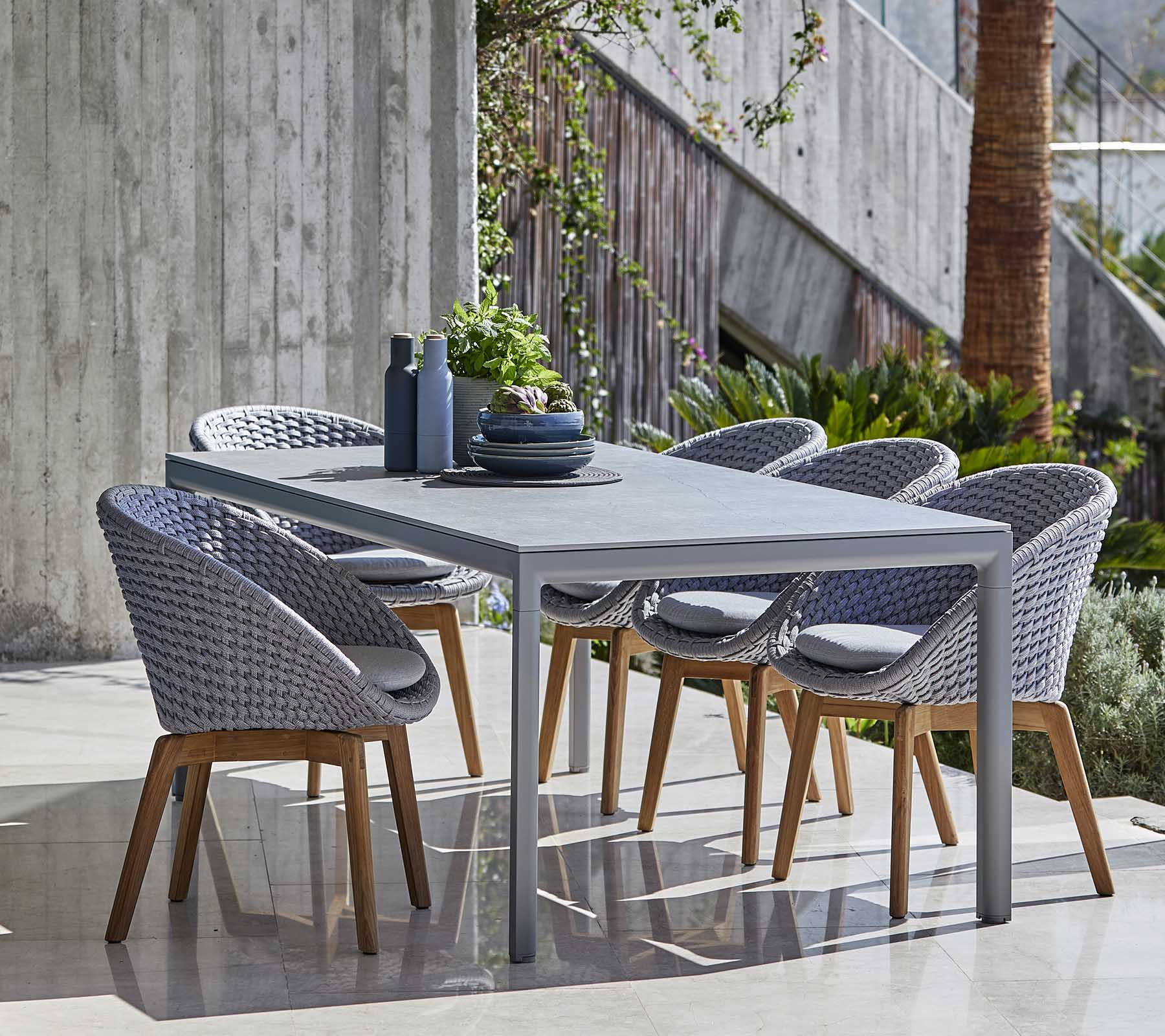 Modern eethoek met een grijze tafel en gevlochten stoelen met houten poten, netjes gerangschikt met decoratieve items op de tafel.