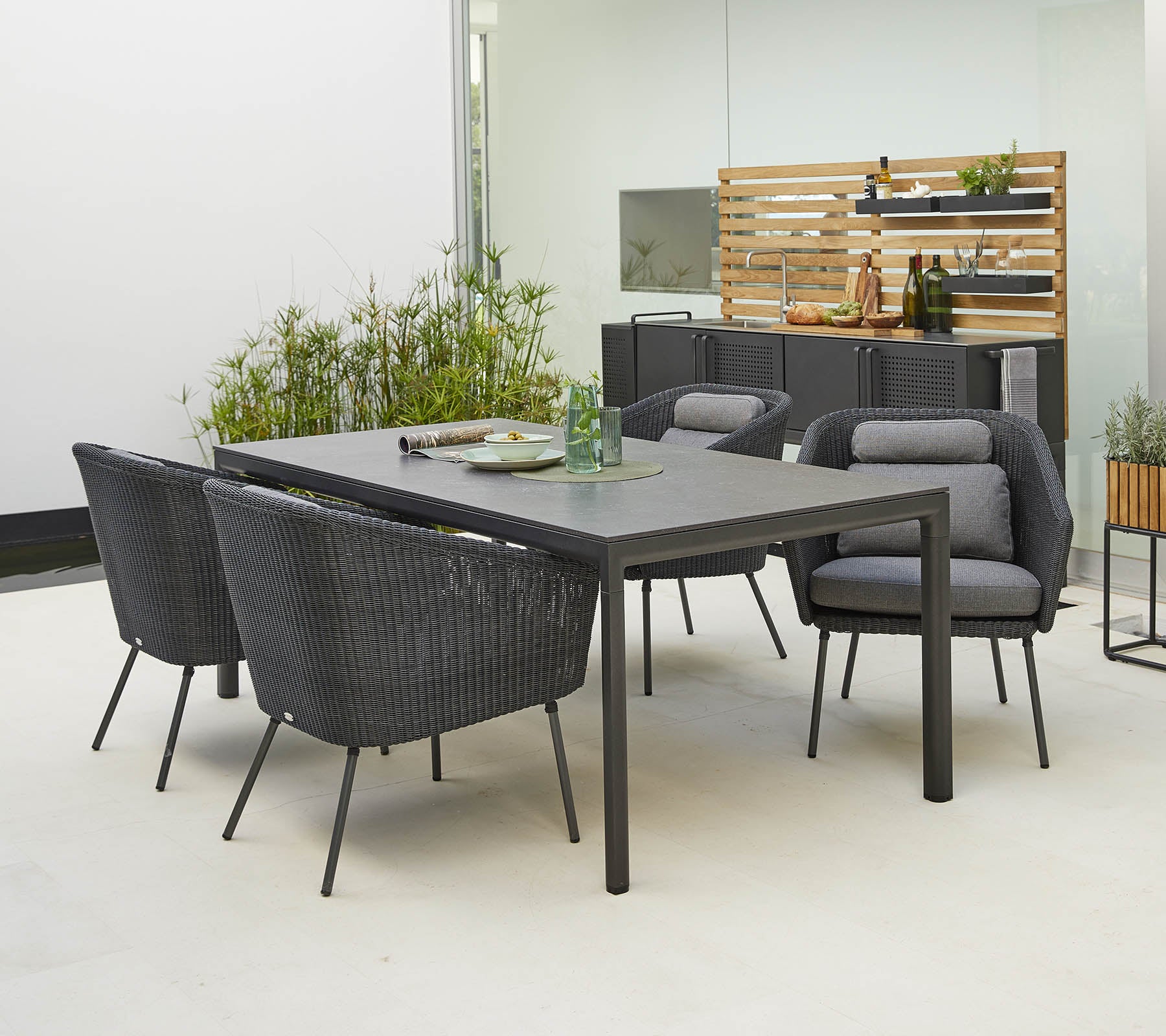 Moderne buitenset met een strak tafel en vier stijlvolle stoelen met comfortabele kussens, omringd door groen.
