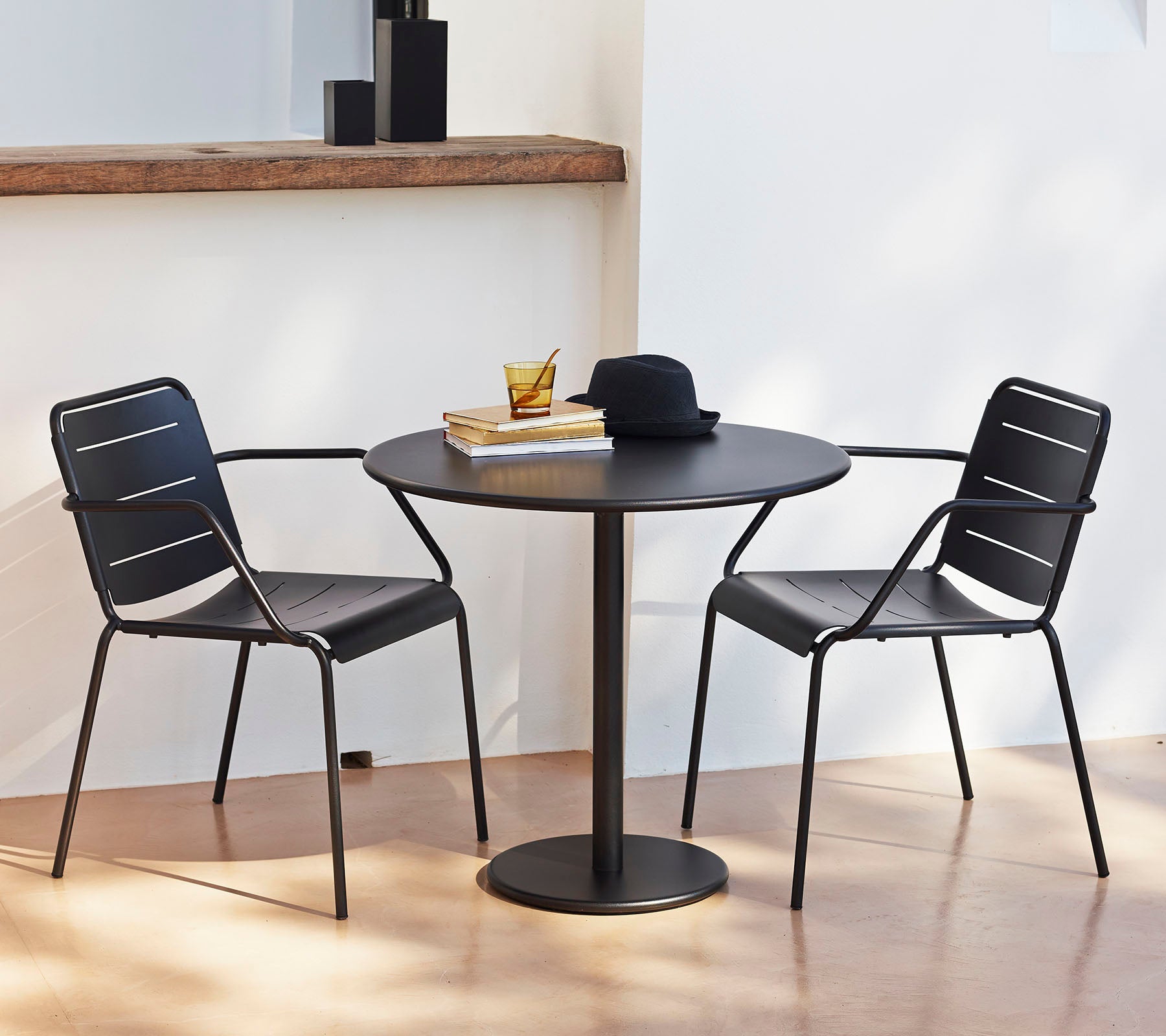 Een rond tafel met twee zwarte stoelen, versierd met een hoed en boeken, die een stijlvolle en uitnodigende zithoek creëert.