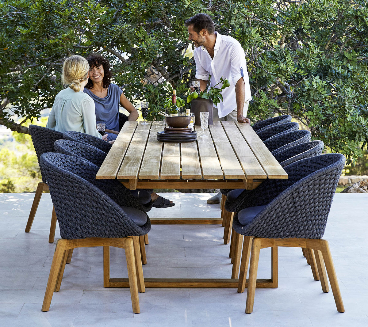 Een stijlvolle eetopstelling met een houten tafel omringd door comfortabele stoelen, met drie mensen die zich in een gesprek verdiepen, te midden van groen.