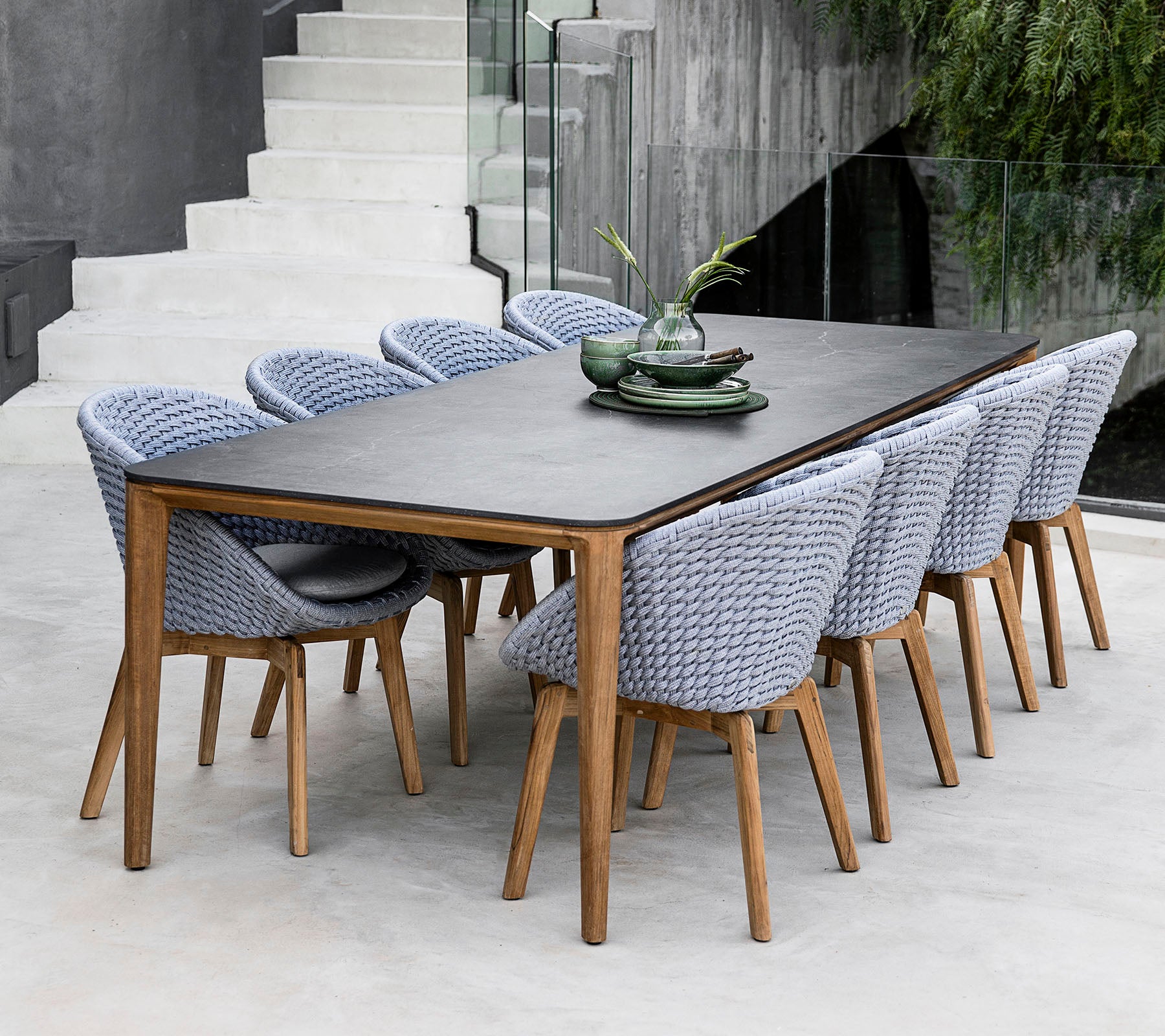Een stijlvol eettafel met een donkere oppervlakte, vergezeld van geweven stoelen in een lichte kleur, aangevuld met decoratieve borden en loof.