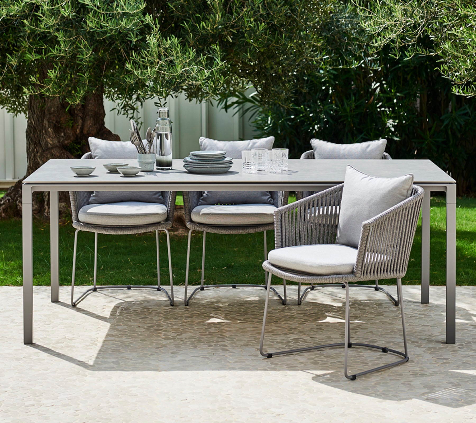 Een moderne buitentafelset met een slank tafel, beklede stoelen en elegant servies, mooi opgemaakt voor een stijlvolle maaltijd.