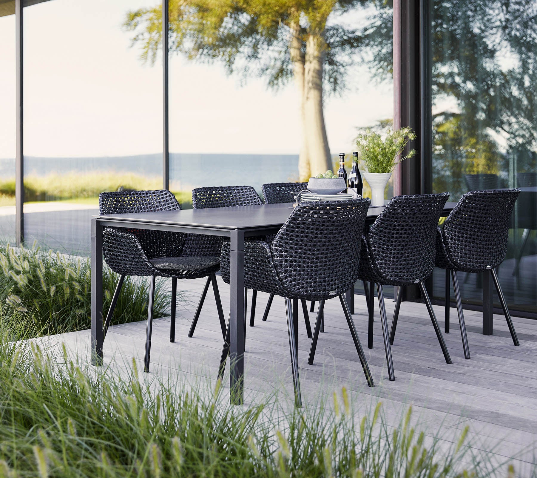 Een stijvol eetset met een zwarte tafel en gevlochten stoelen, omgeven door weelderig groen en uitgestrekte uitzichten. Ideaal voor bijeenkomsten.
