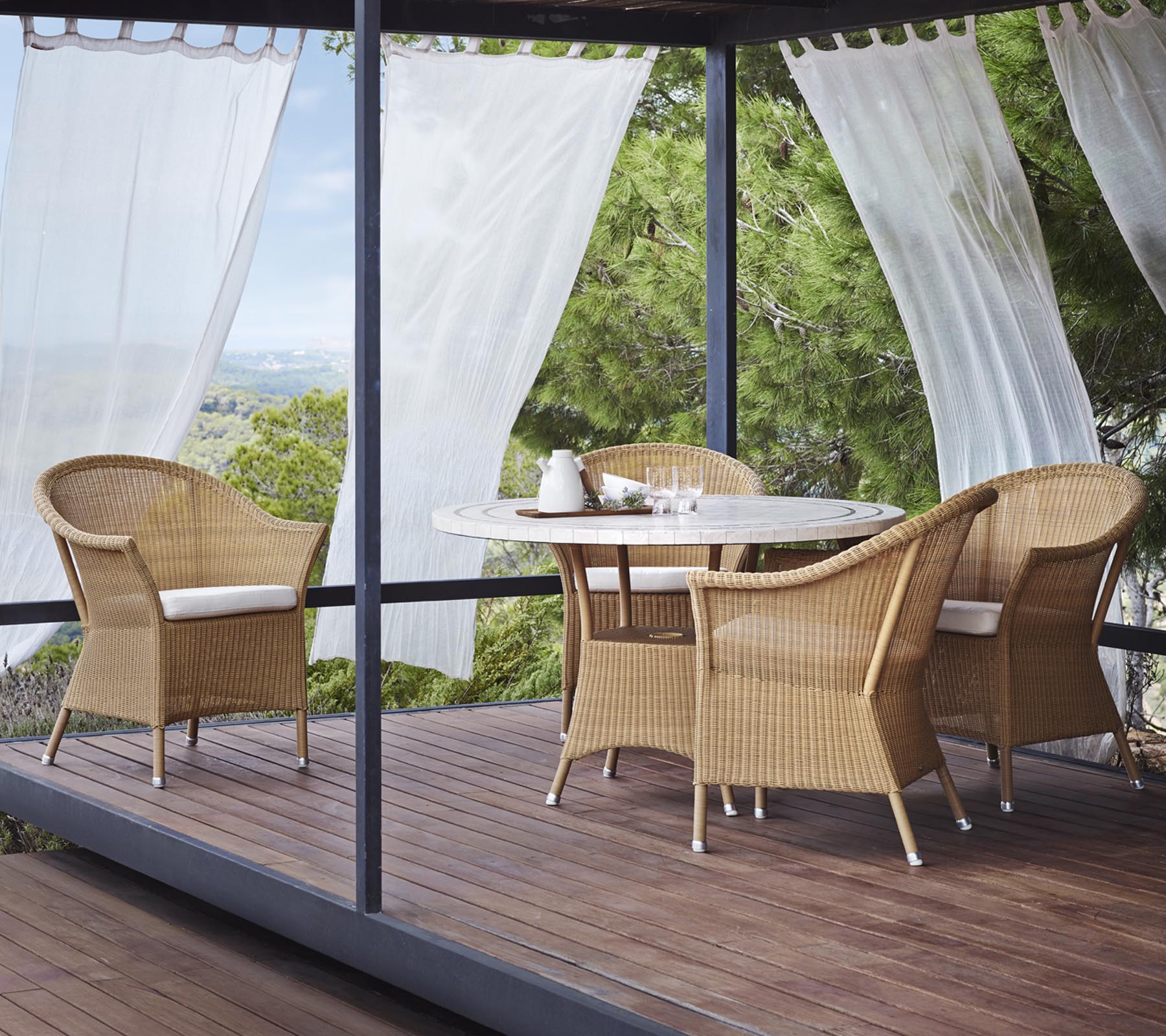 Een stijlvol zitgedeelte met vier wicker stoelen en een ronde tafel, omringd door sheer gordijnen en natuurlijke begroeiing.