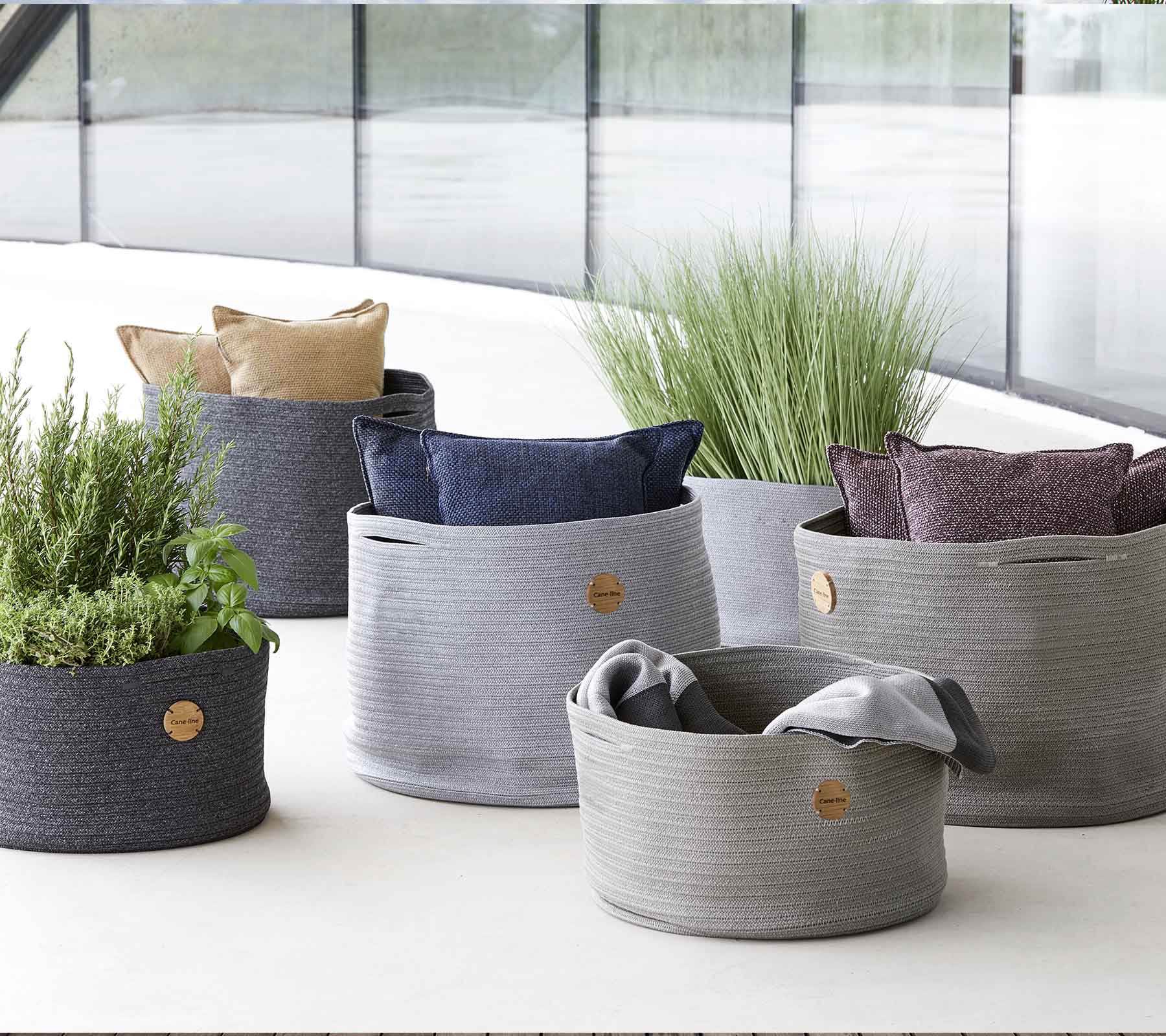 Een verscheidenheid aan stijlvolle geweven opbergmanden in verschillende maten, met levendige kussens en groen voor een decoratieve touch.