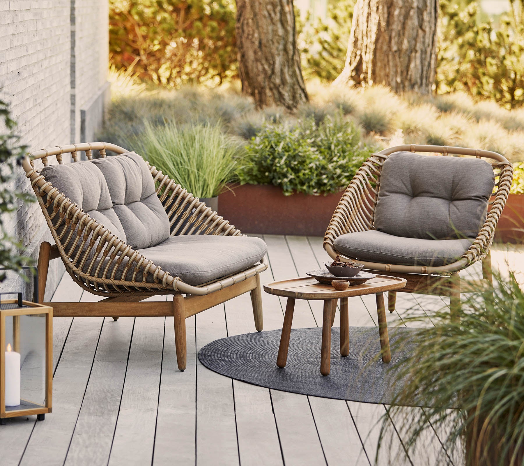 Twee stijlvolle stoelen met zachte kussens omringen een klein houten tafeltje op een gestructureerd oppervlak, aangevuld met groene planten op de achtergrond.