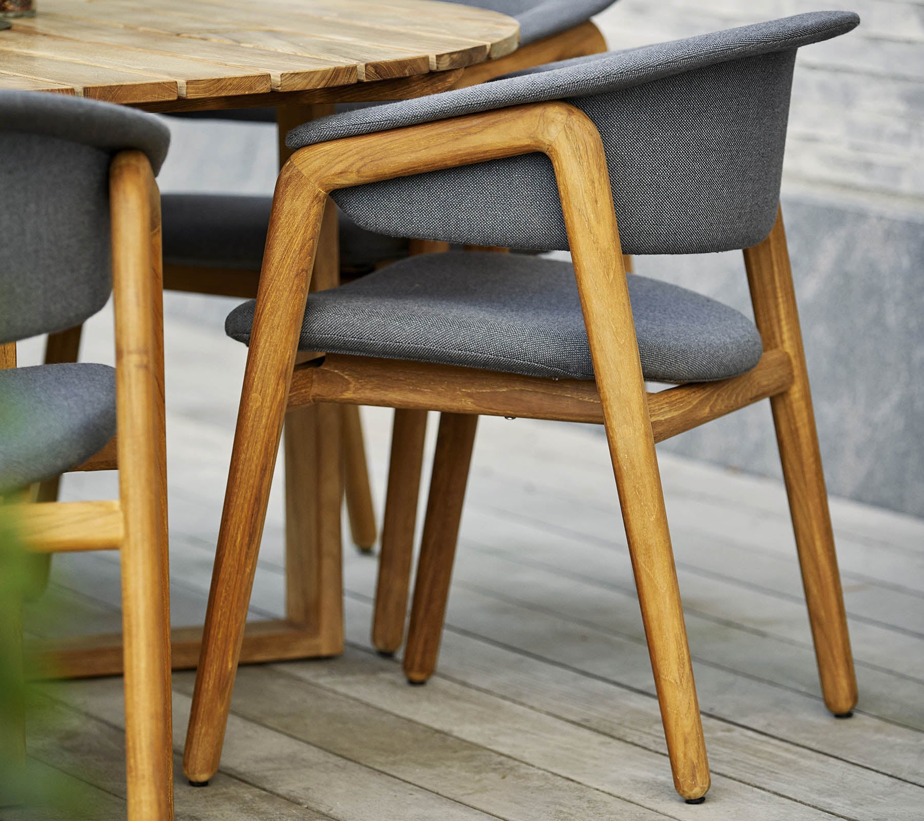 Stijlvolle houten stoel met grijs gestoffeerde zitting en rugleuning, gecombineerd met een ronde tafel in een hedendaags ontwerp.