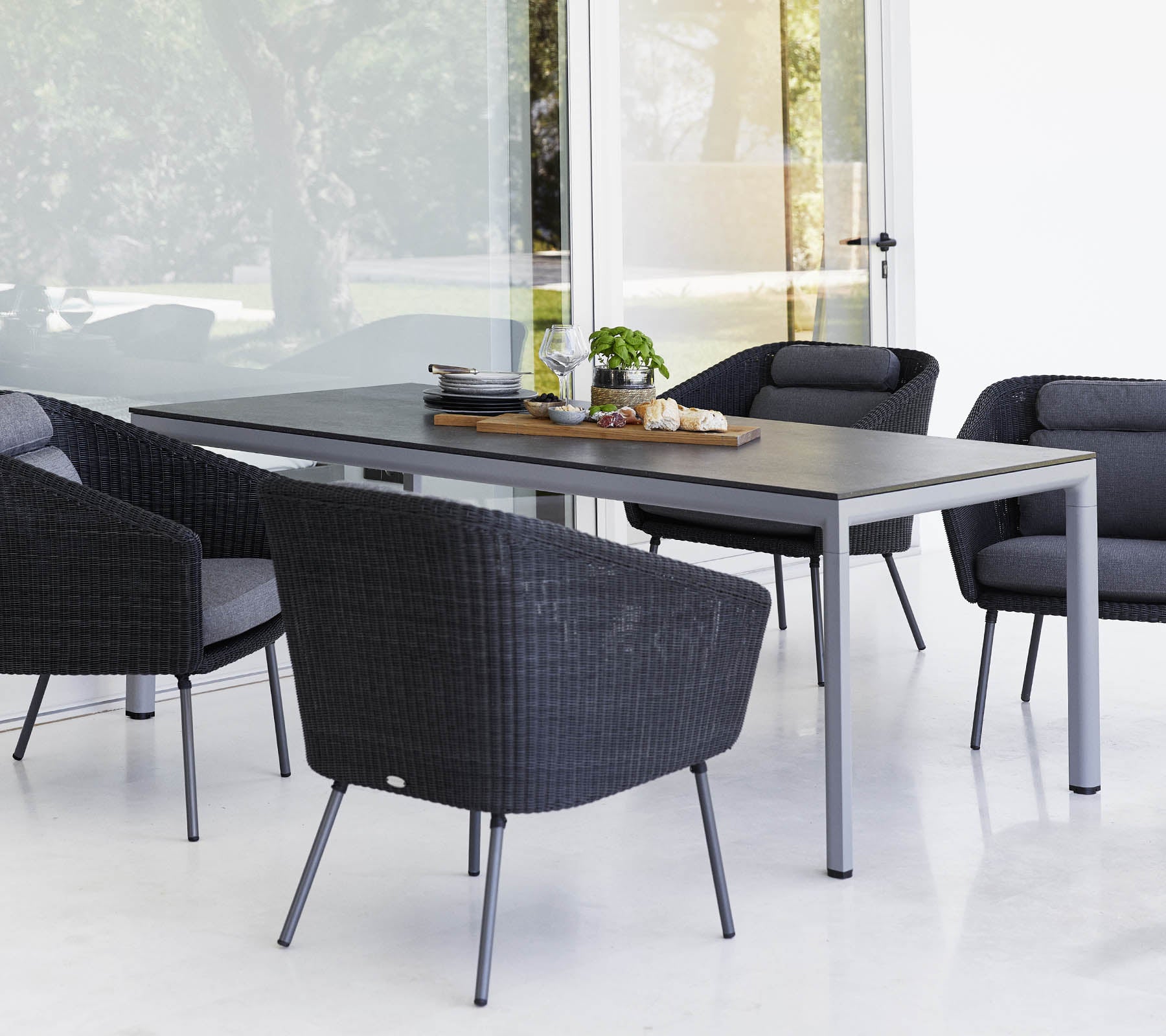 Een moderne eettafel omgeven door vier stijlvolle zwarte buitenstoelen, met een middenstuk en groen op de tafel.