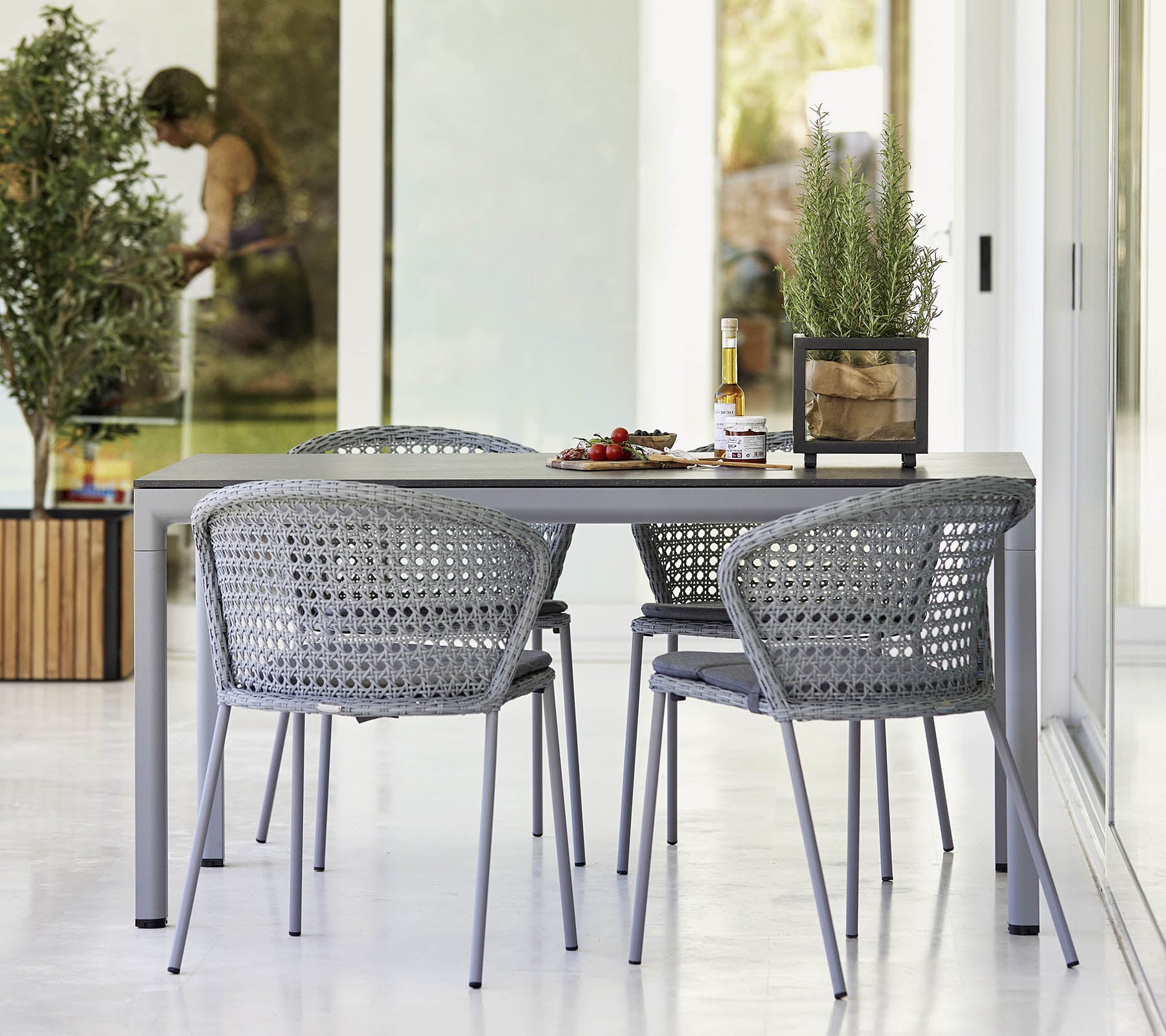 Moderne eettafelset met een slank tafel en gevlochten stoelen, aangevuld met groen en een lichte, luchtige sfeer.