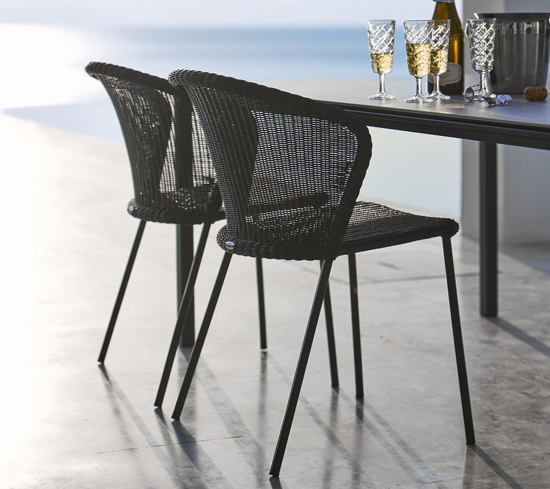 Twee stijlvolle zwarte gevlochten stoelen naast een tafel gedekt met glazen en een fles, die een ontspannen eet sfeer oproept.