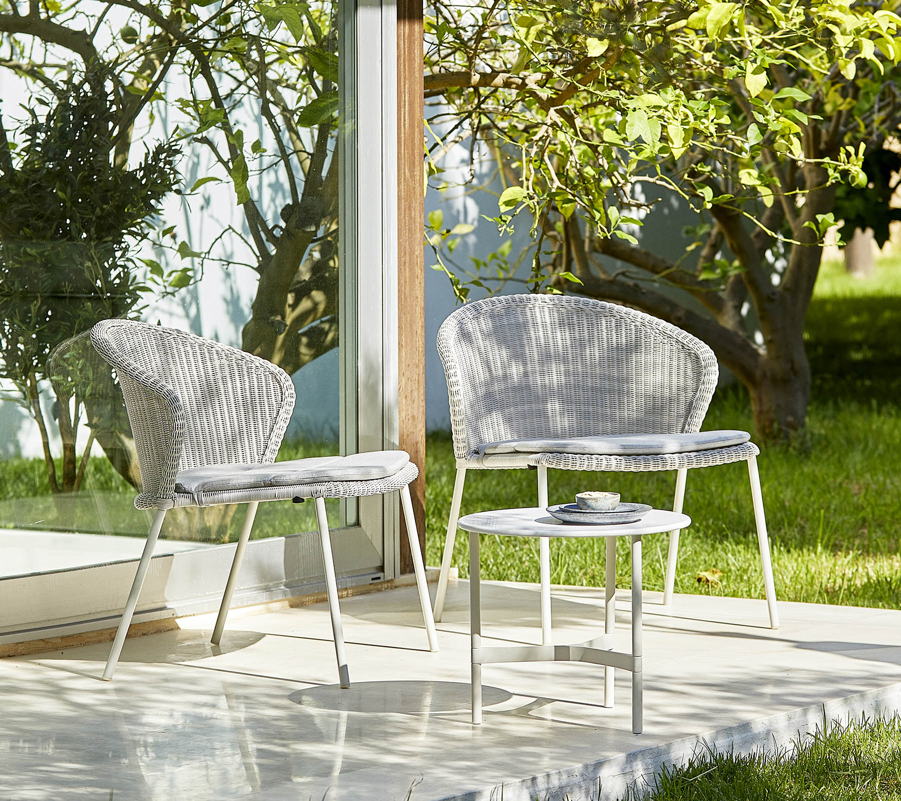Twee stijlvolle stoelen en een kleine tafel in een serene setting met groen, perfect voor ontspanning en buitenbijeenkomsten.
