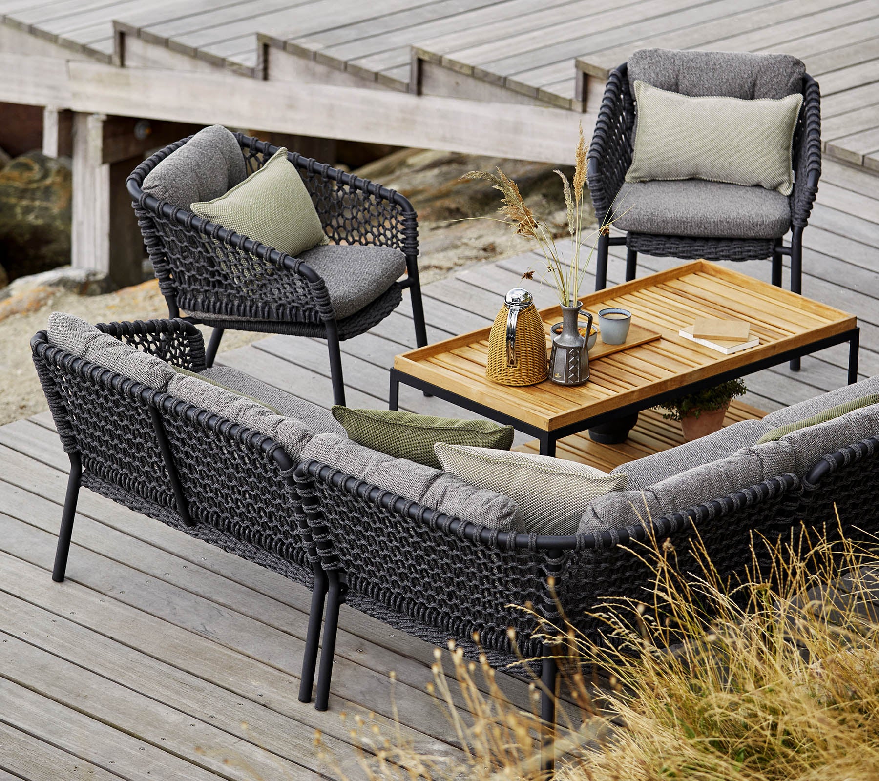 Stijlvolle buitenset met een gezellige bank, twee stoelen en een houten salontafel, aangevuld met zachte kussens en decoratieve items.