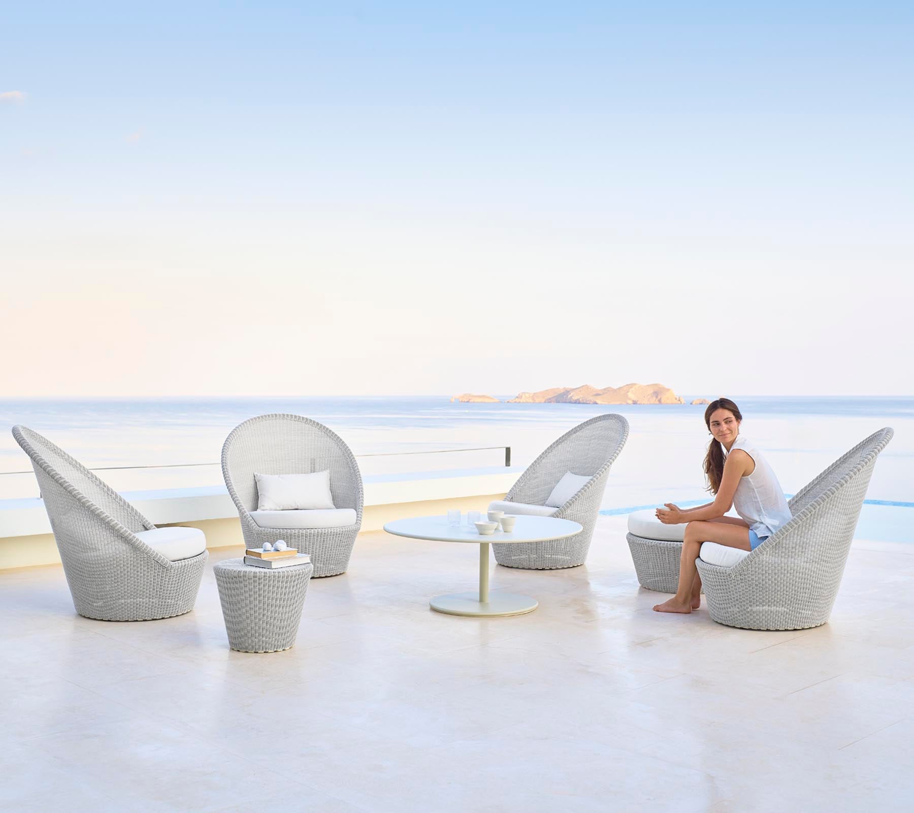Een stijlvolle zitarrangement met elegante stoelen en een tafel, met een vrouw die gracieus zit bij een serene waterachtergrond.