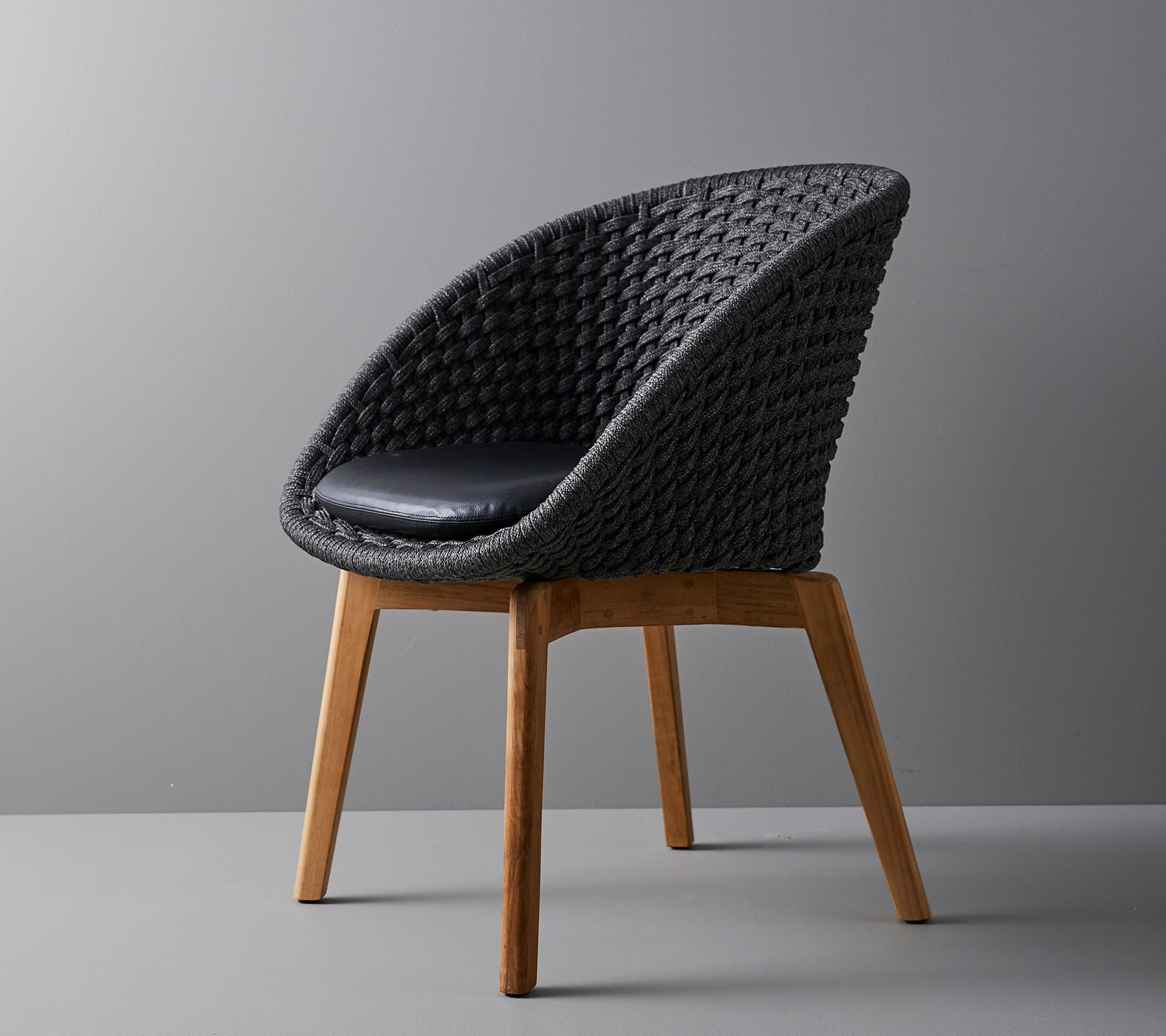 Stijlvolle geweven stoel met een comfortabel kussen, met coole, taps toelopende houten poten en een modern ontwerp dat geschikt is voor verschillende omgevingen.