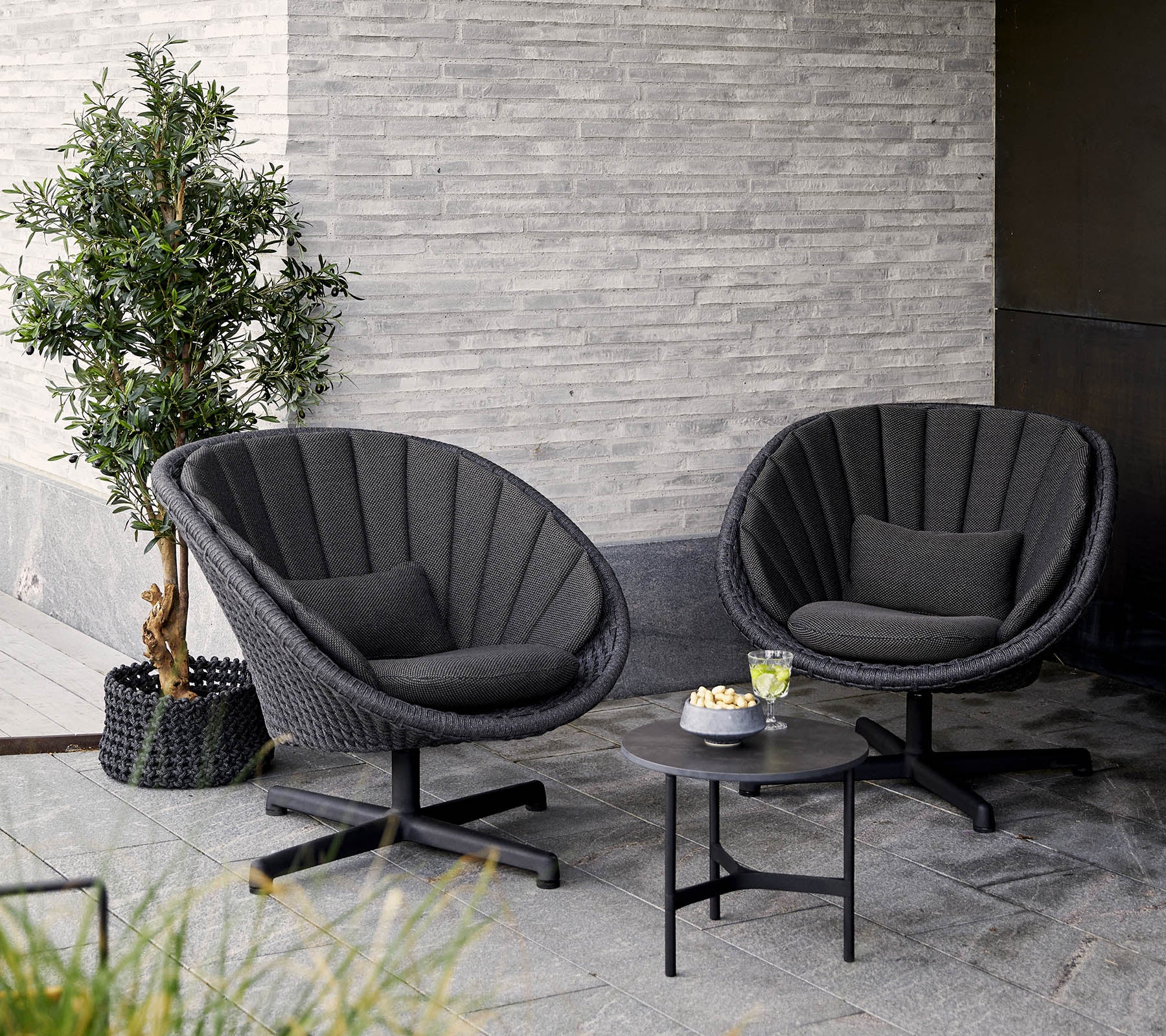 Twee stijlvolle, moderne stoelen met een rond ontwerp, vergezeld van een klein tafeltje en een potplant, voor een gestructureerde muur.
