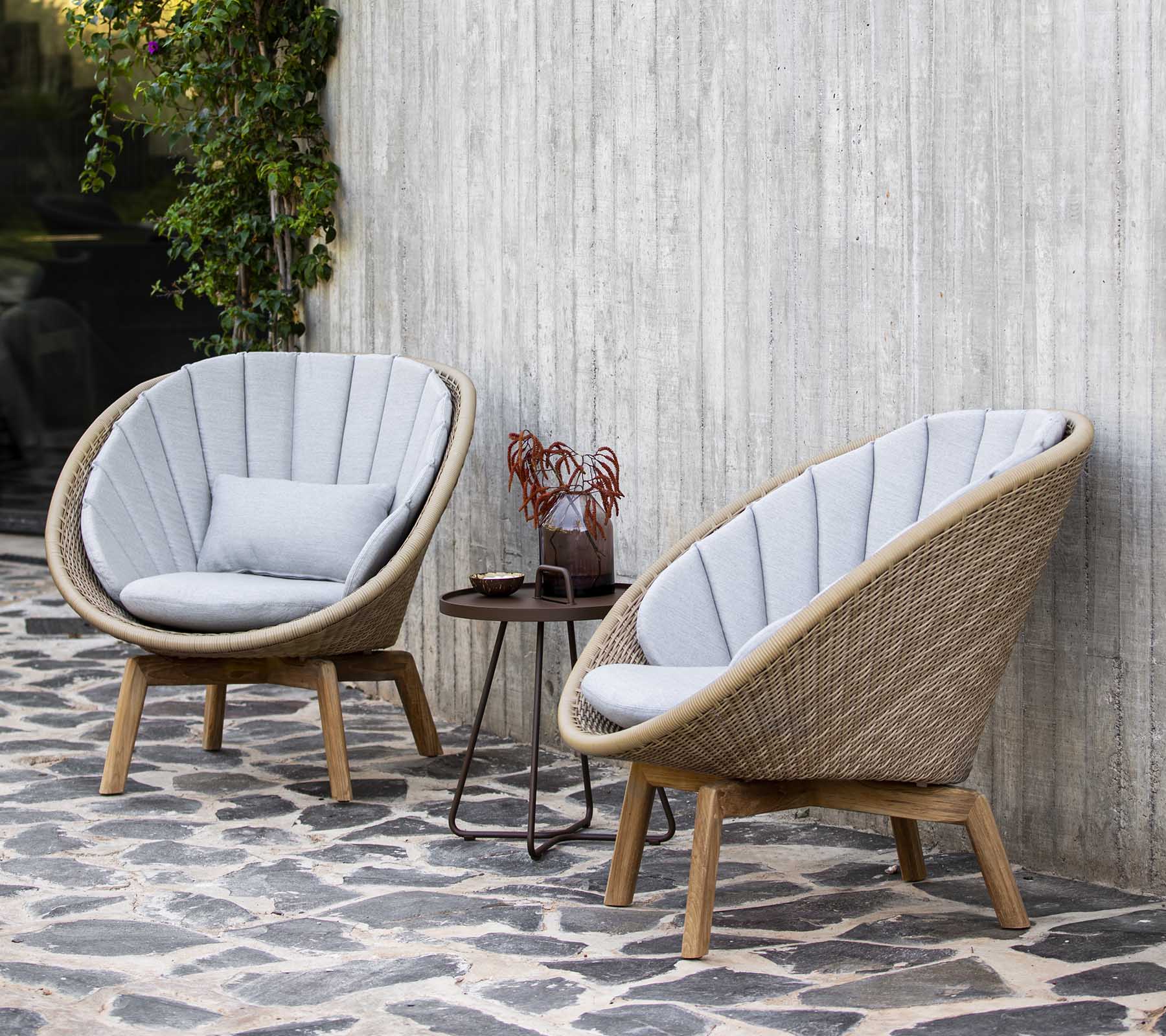 Twee stijlvolle, gebogen fauteuils met zachte grijze kussens naast een klein tafeltje versierd met decoratieve items, geplaatst tegen een gestructureerde muur.