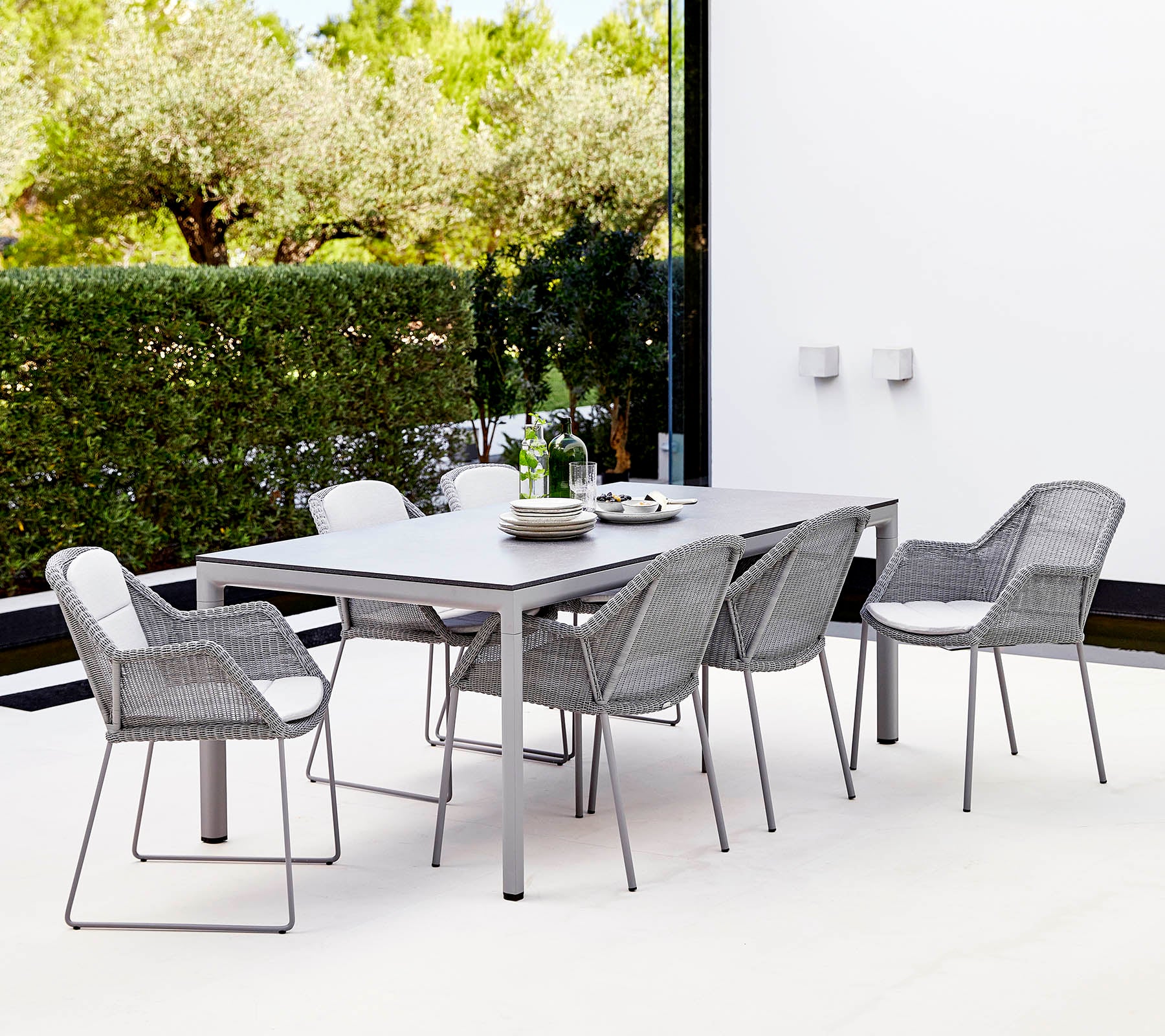 Een moderne eettafel met een rechthoekige tafel en zes stijlvolle gevlochten stoelen, omringd door groen.