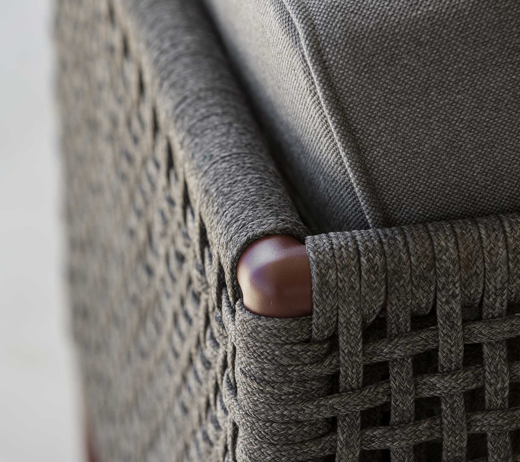 Close-up van een geweven meubelhoek met elegant grijs stoffen en gladde houten accenten, die een mix van textuur en stijl laat zien.