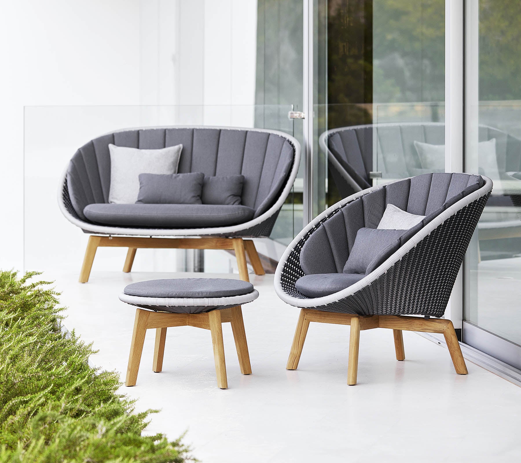 Stijlvolle zithoek met een gebogen bank, stoel en ronde salontafel, allemaal met een modern design en zachte grijze kussens.