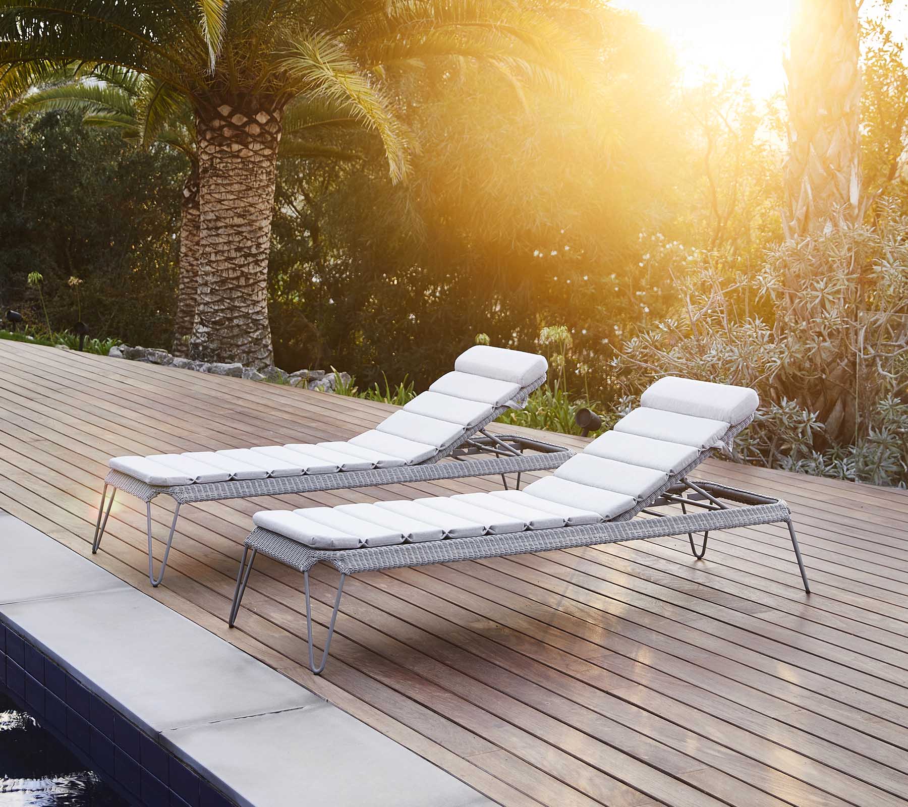 Twee stijlvolle loungestoelen met witte kussens, naast een zwembad geplaatst en omringd door weelderig groen, genietend van het warme zonlicht.