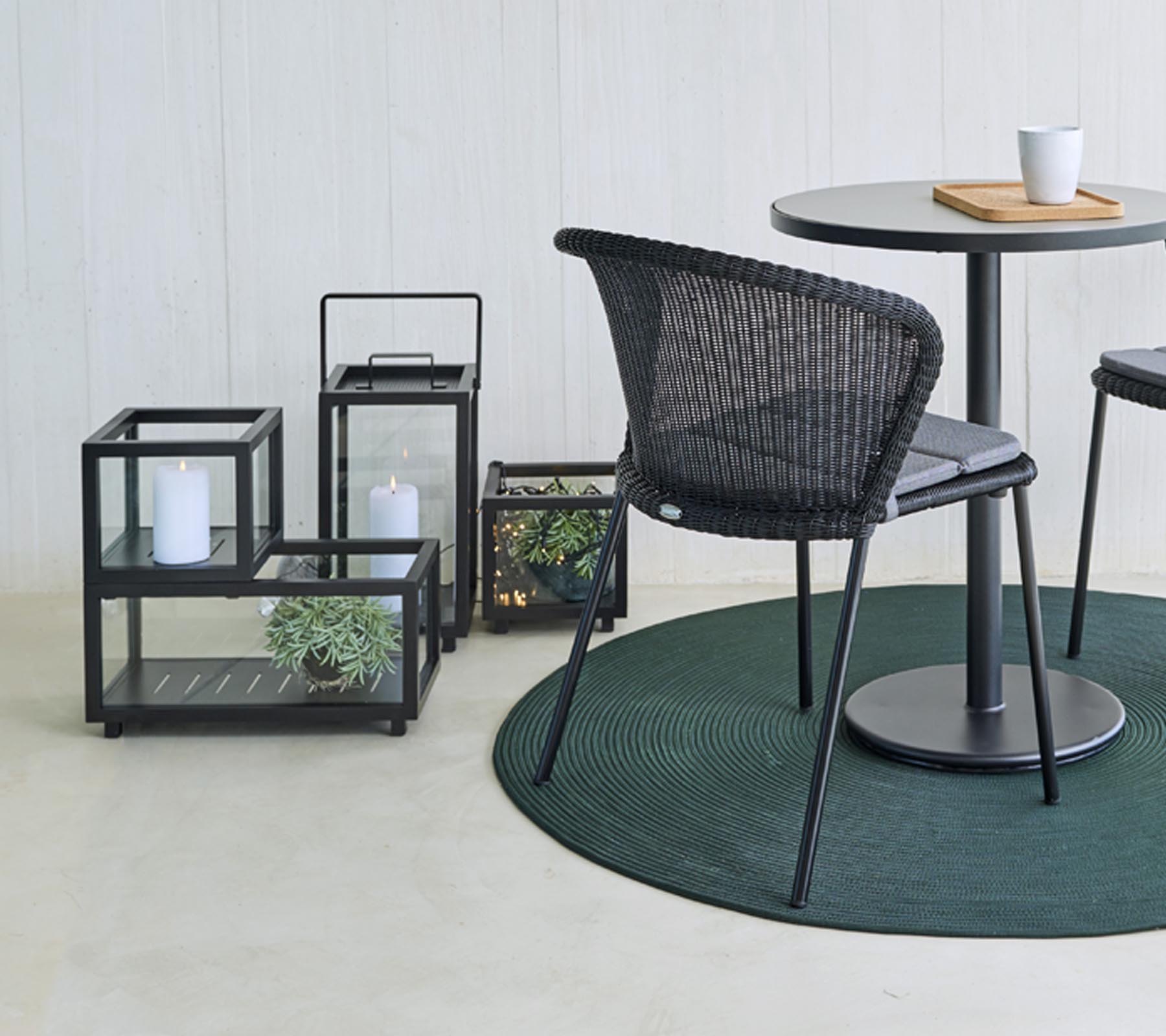 Moderne zitplaatsen en decoratieve glazen lantaarns met planten, rondom een ronde tafel, op een rond groen tapijt.