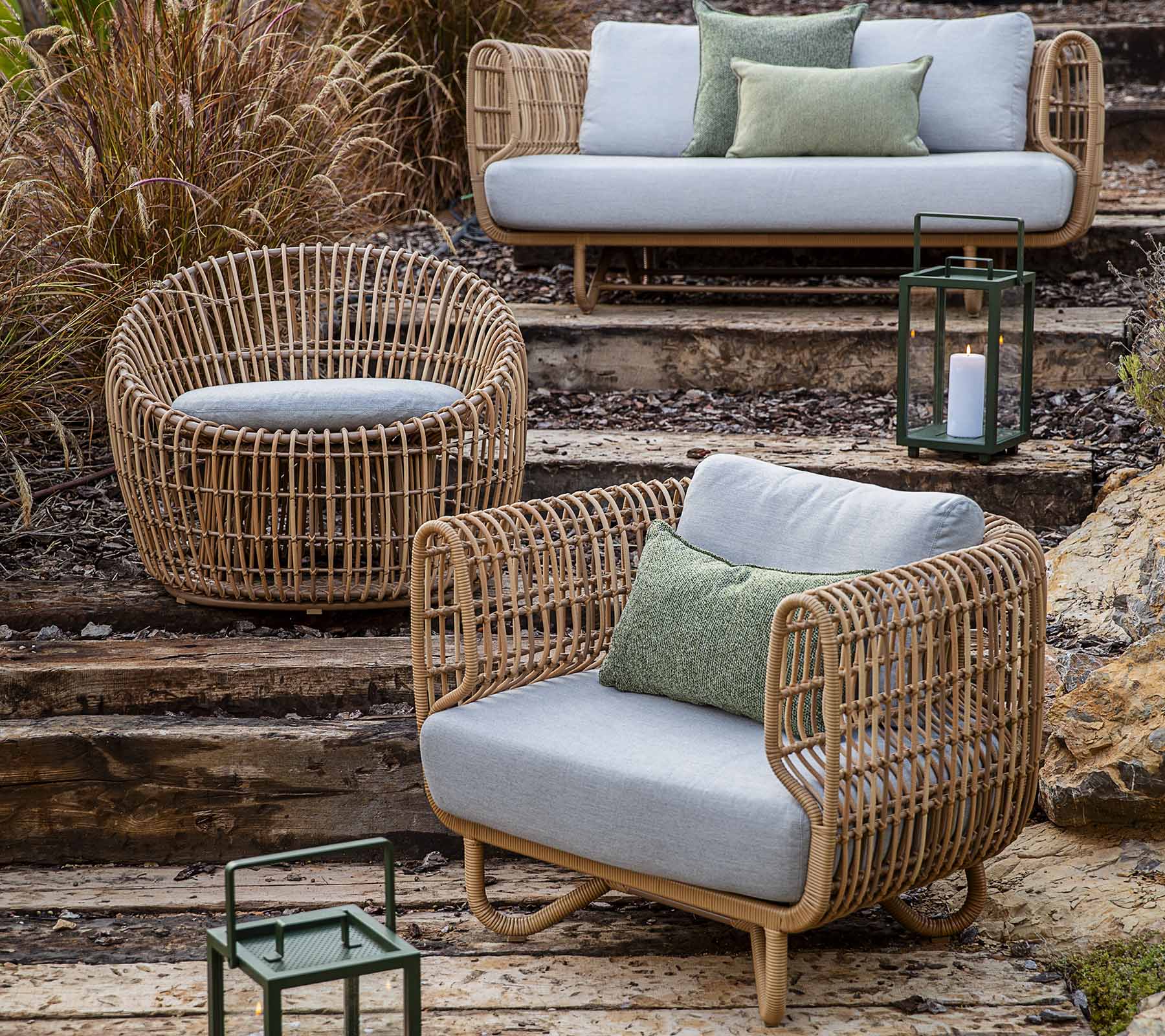 Een collectie van geweven wicker meubels, inclusief een bank, stoel en rond zitmeubel, geaccentueerd met kussens en lantaarns.