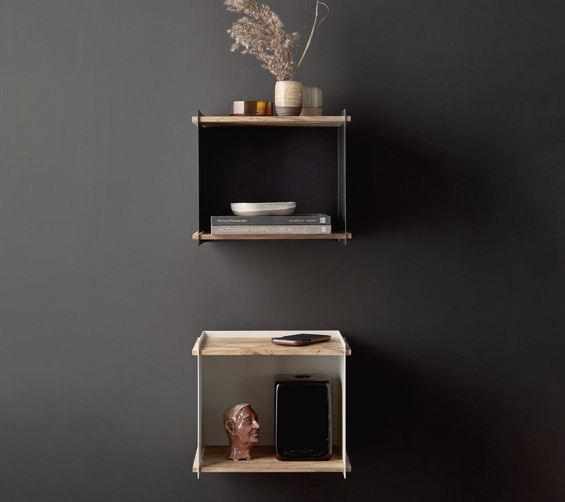 Stijlvolle wandplanken met decoratieve items, waaronder een vaas met gedroogde bloemen, een schaal en een klein beeldhouwwerk, tegen een donkere achtergrond.