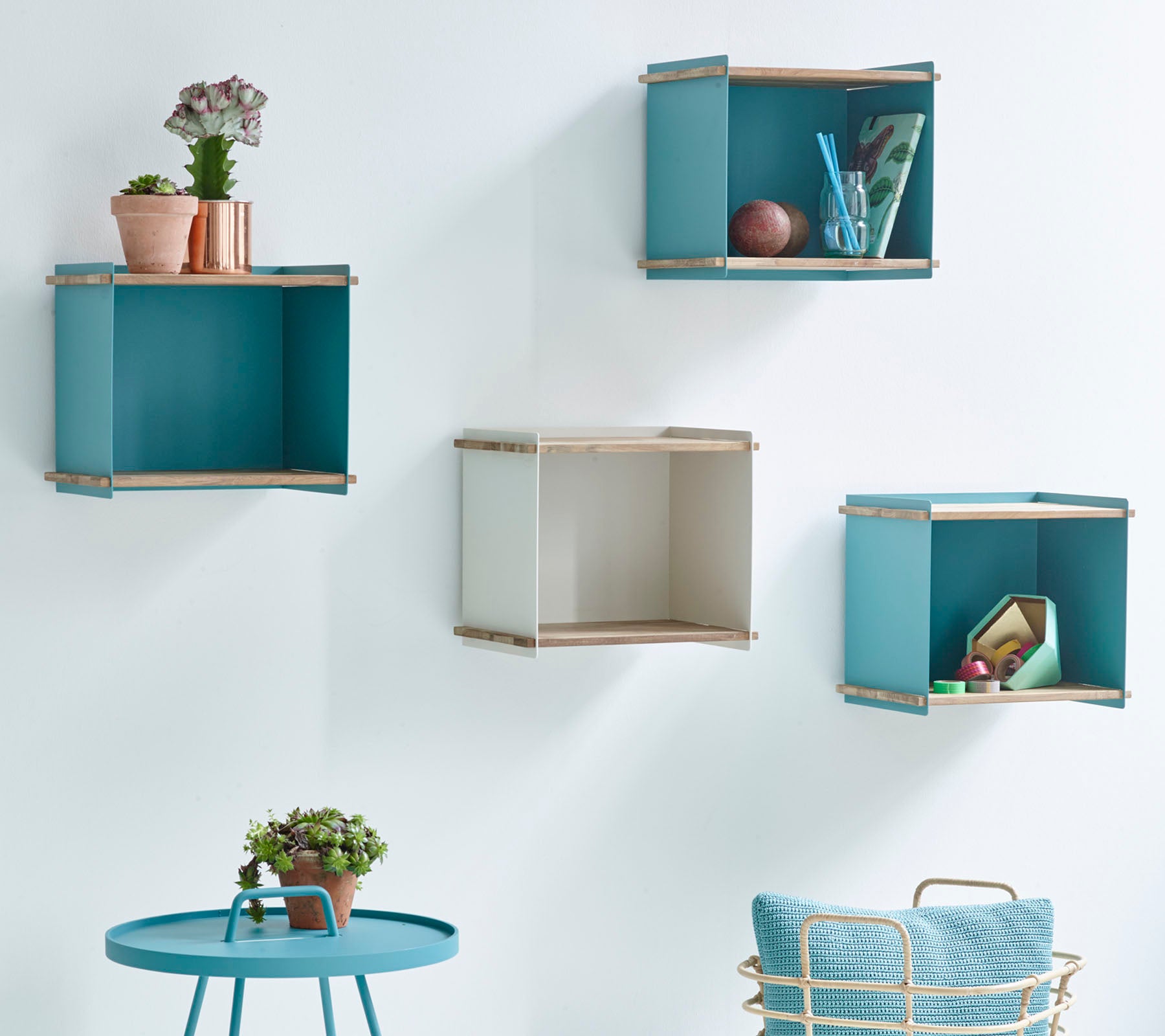 Vier decoratieve wandgemonteerde opbergdozen in blauw en beige, vergezeld van een kleine ronde tafel met een geplante plant.