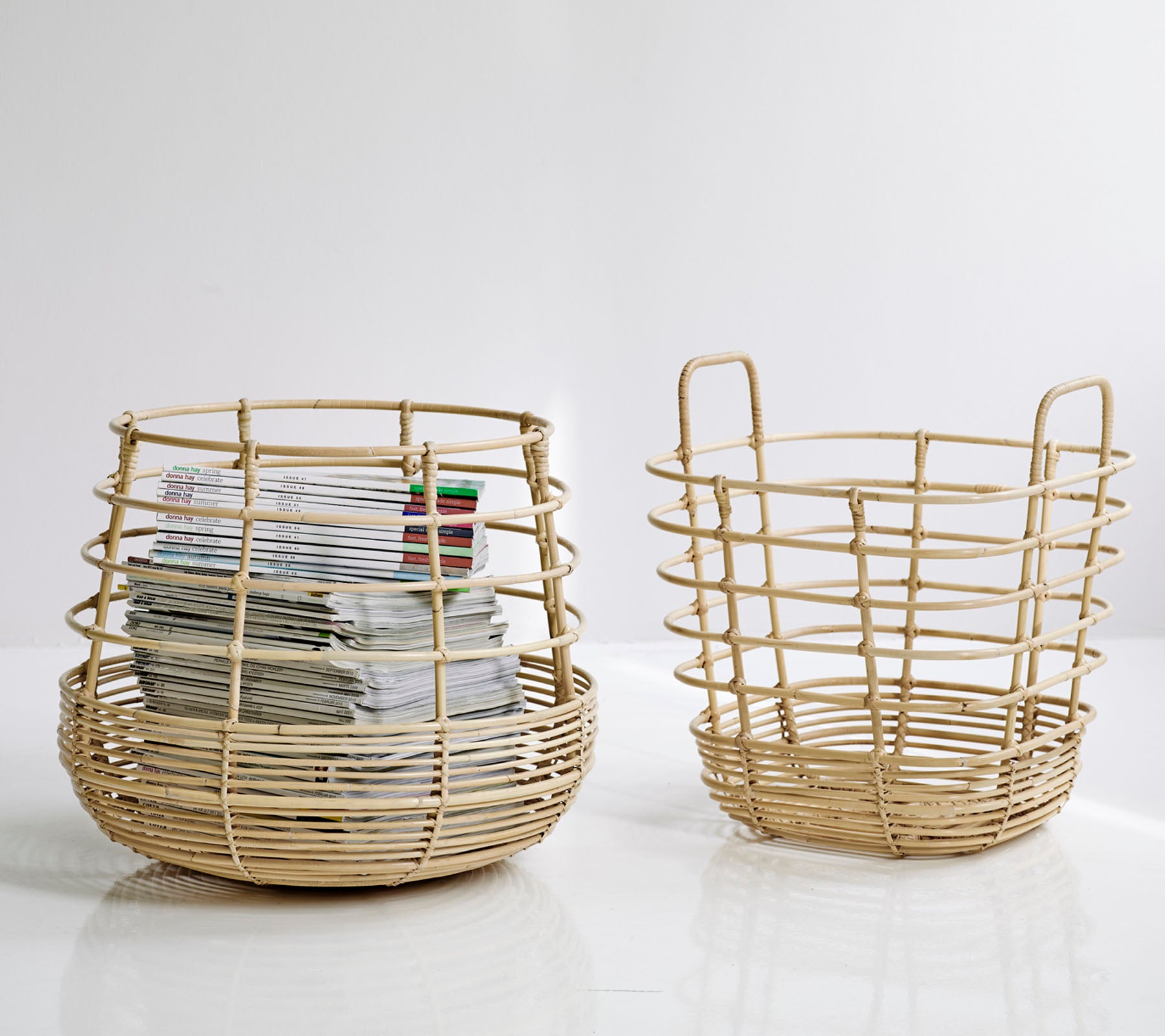 Twee geweven opbergmanden, één groter en rond met papieren erin, en een kleinere, open ontwerp ernaast, beide in een natuurlijke kleur.