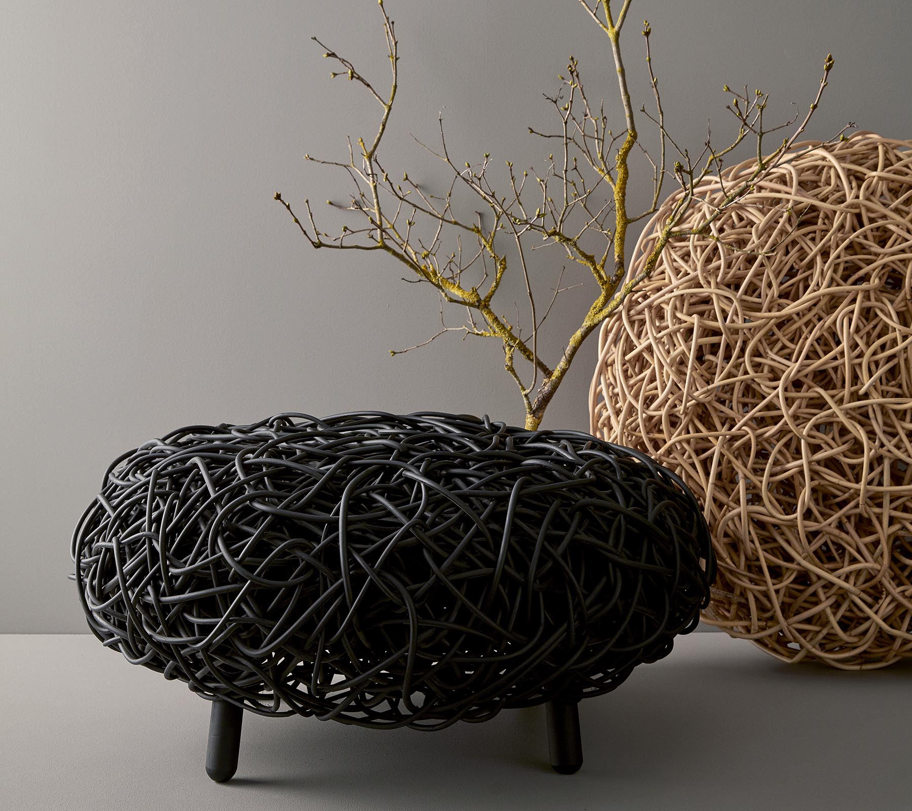 Een stijlvolle, ronde salontafel van geweven materiaal, in zwart en natuurlijke tinten, met een decoratieve tak bovenop.
