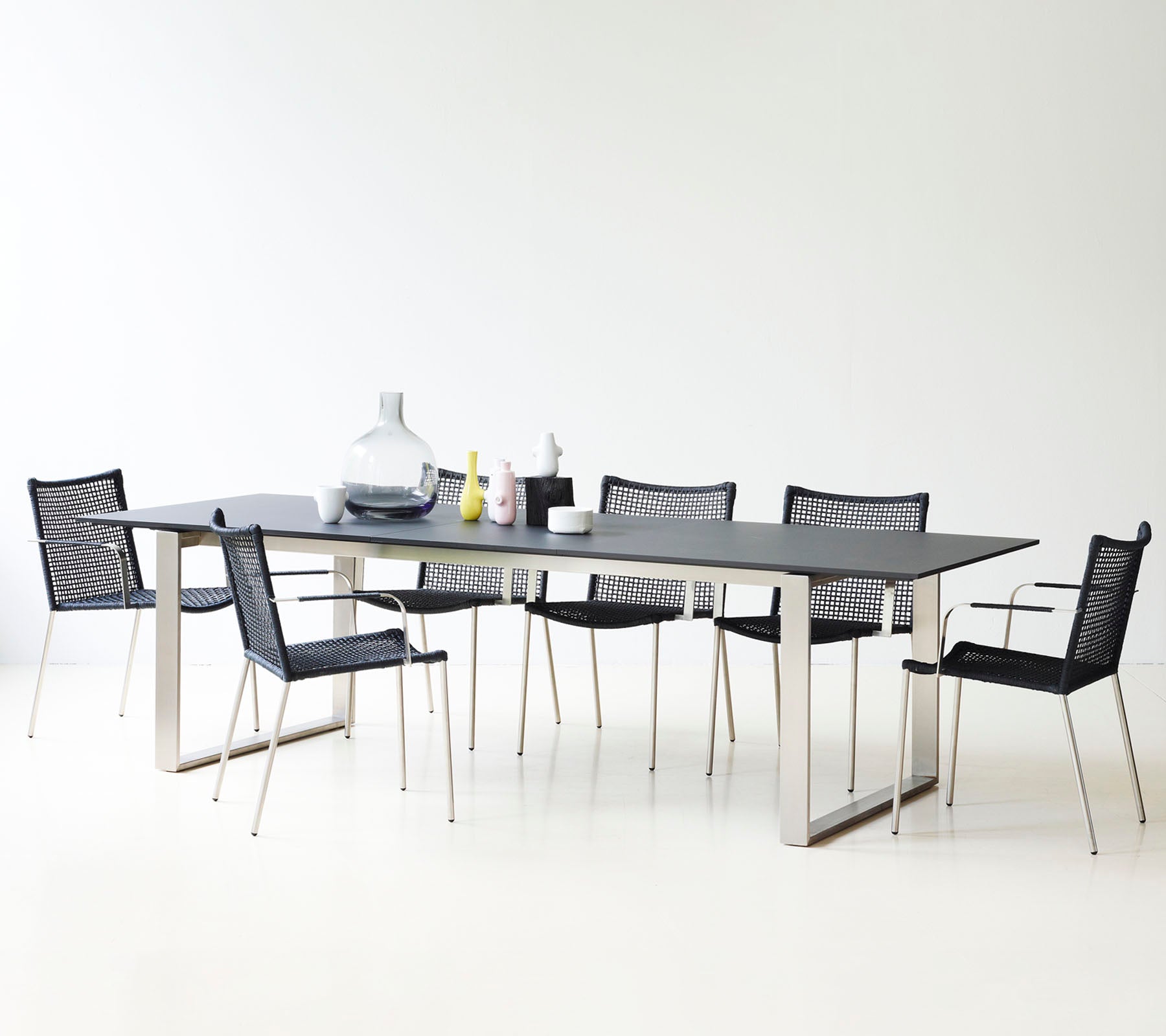 Een moderne eettafel met een slank ontwerp, omringd door stijlvolle zwarte mesh-stoelen en decoratieve vazen.