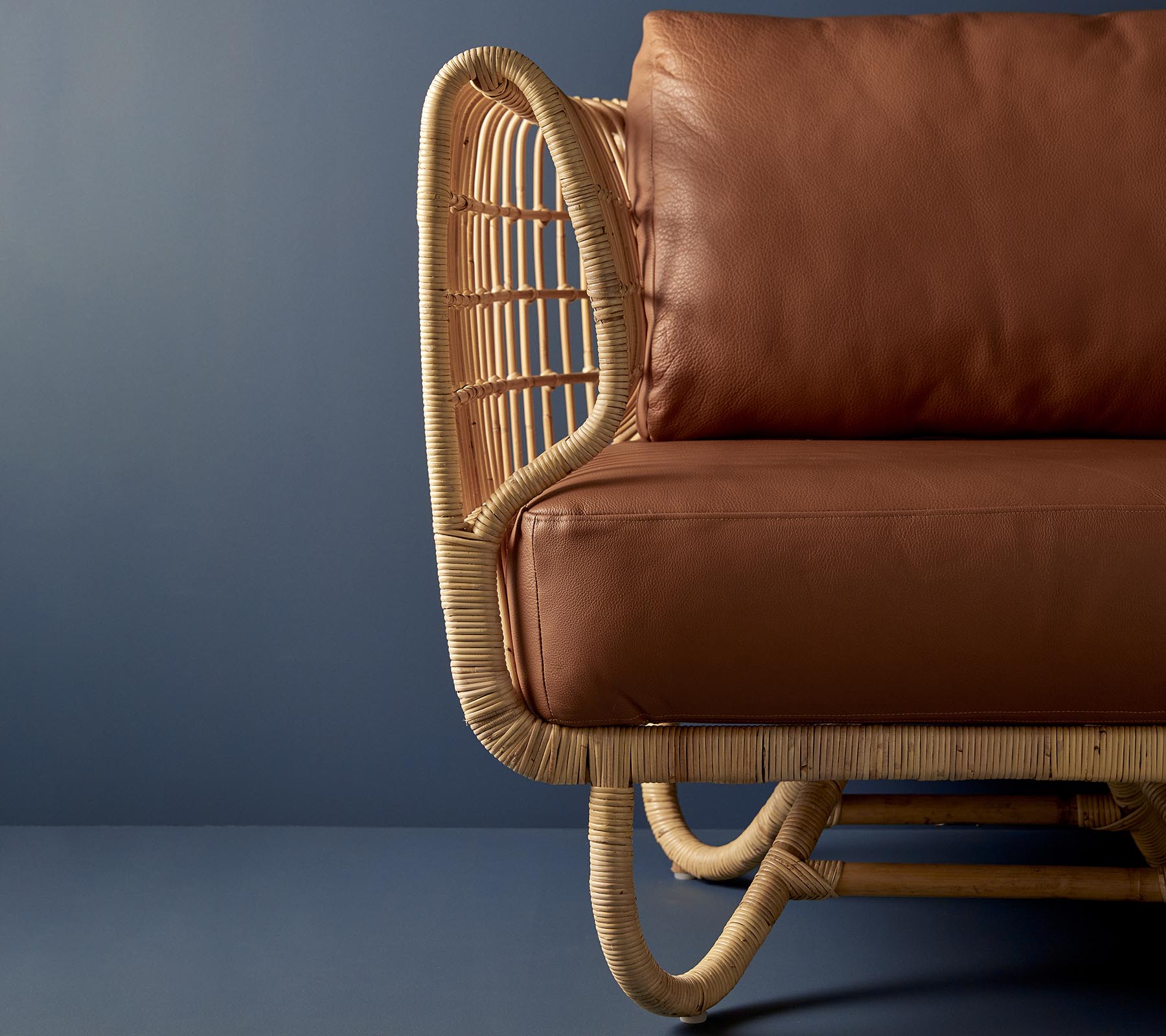Rattenstoel met een gebogen ontwerp en bruine leren kussens, die een combinatie van natuurlijke materialen en moderne esthetiek toont.