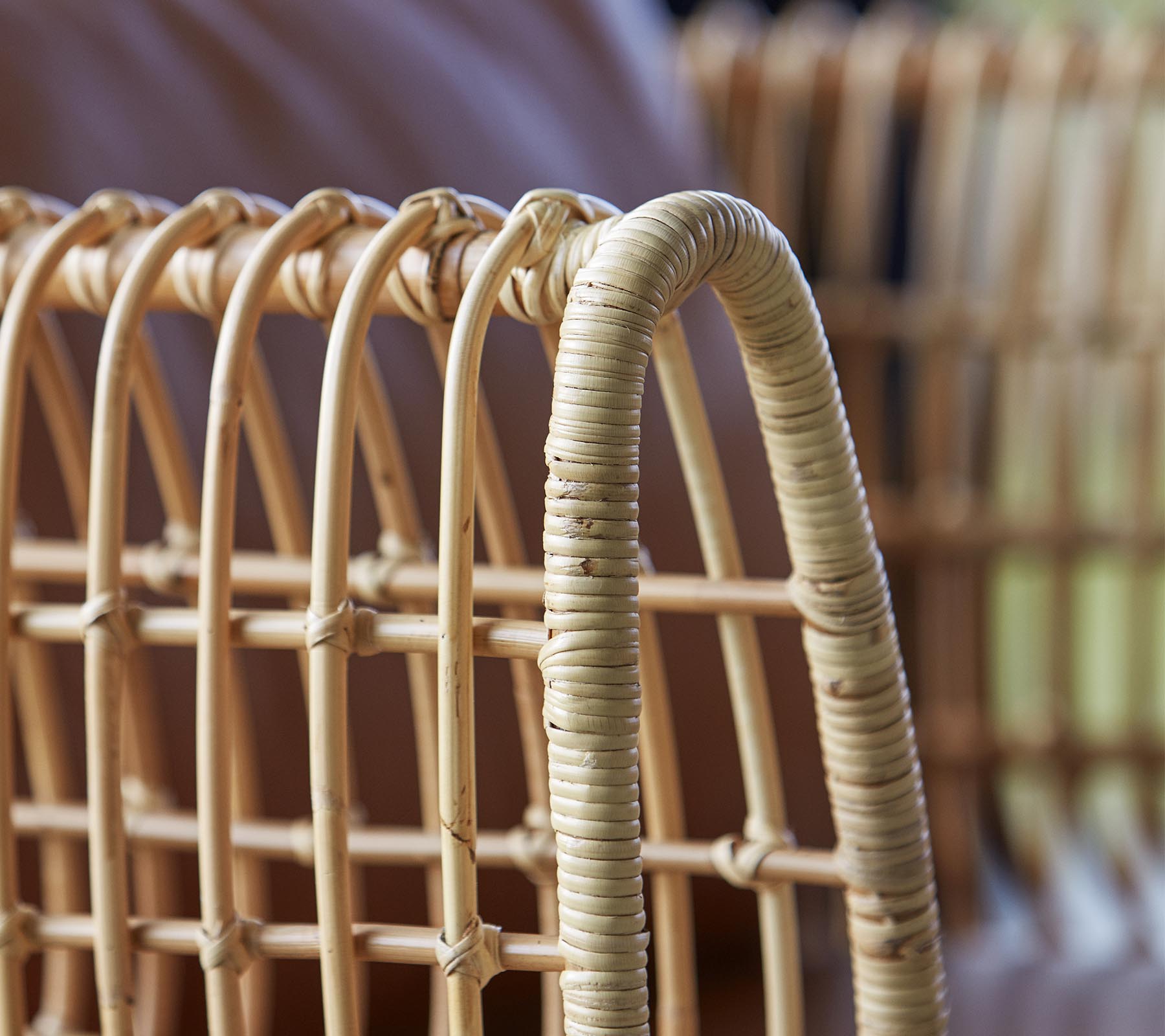 Close-up van een geweven rotan stoel met gebogen lijnen en een natuurlijke afwerking, die het vakmanschap en design benadrukt.