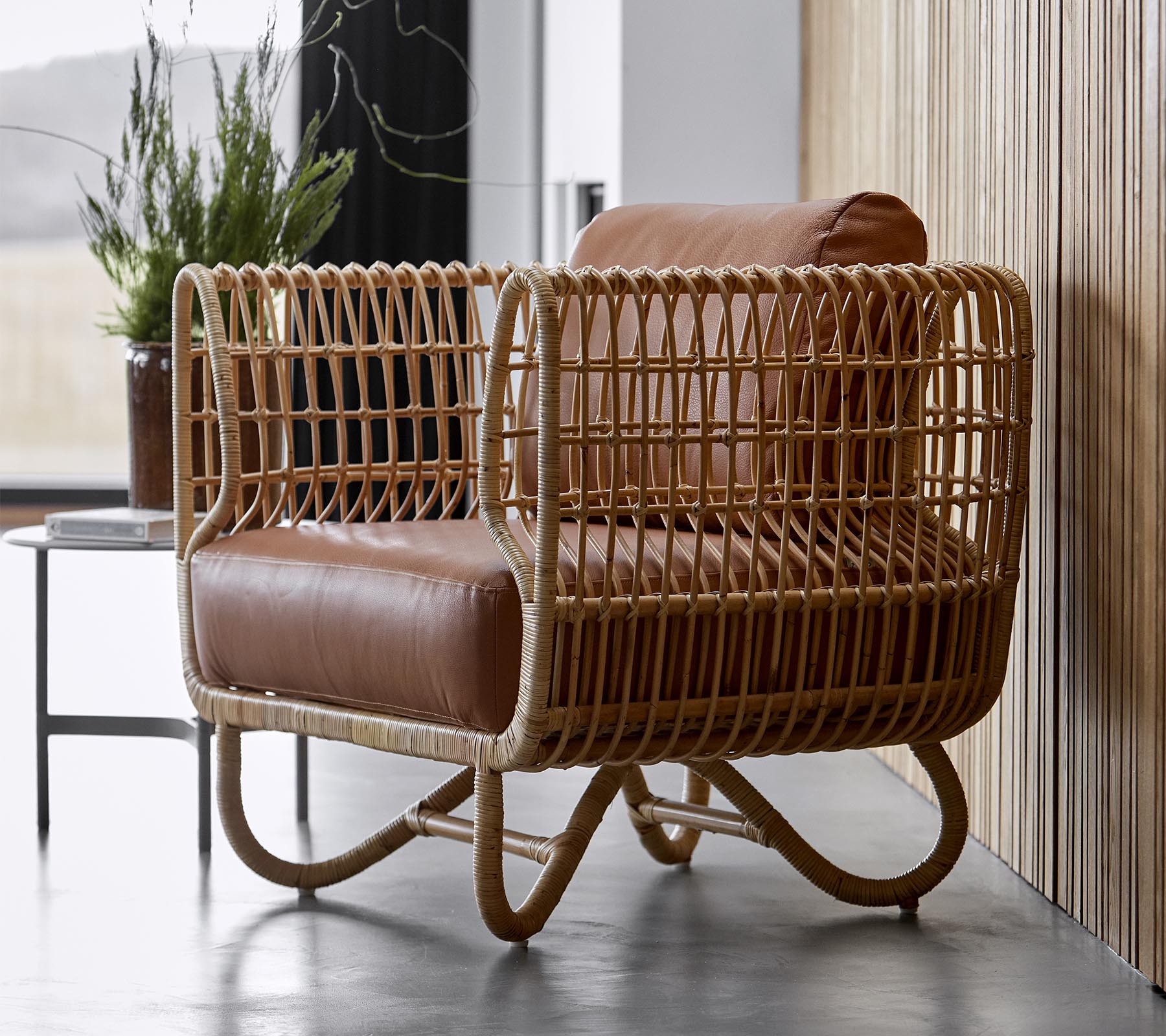 Stijlvolle fauteuil met een gevlochten rieten frame en zachte bruine leren kussens, perfect voor moderne decoratie.
