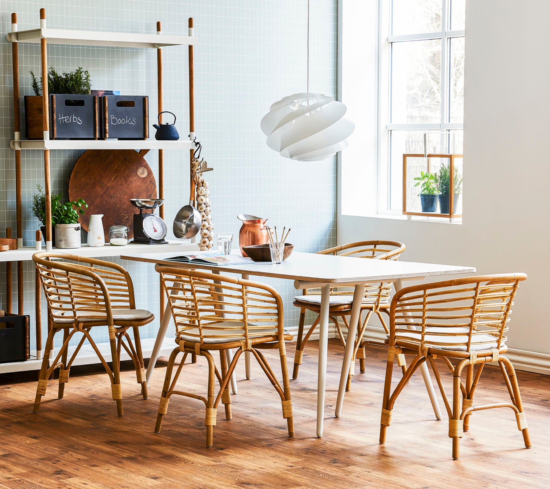 Een stijlvolle eetruimte met een licht houten tafel omringd door rattanstoelen en een moderne hanglamp, aangevuld met decoratieve planken.