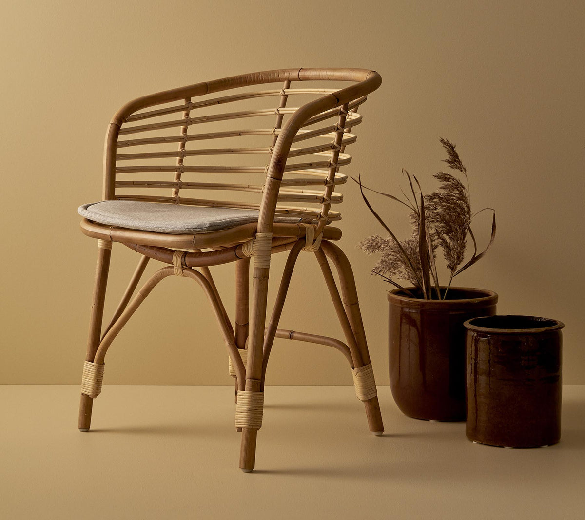 Een stijlvolle rieten stoel met een gewatteerde zitting, vergezeld van twee decoratieve plantenpotten met gedroogde planten.