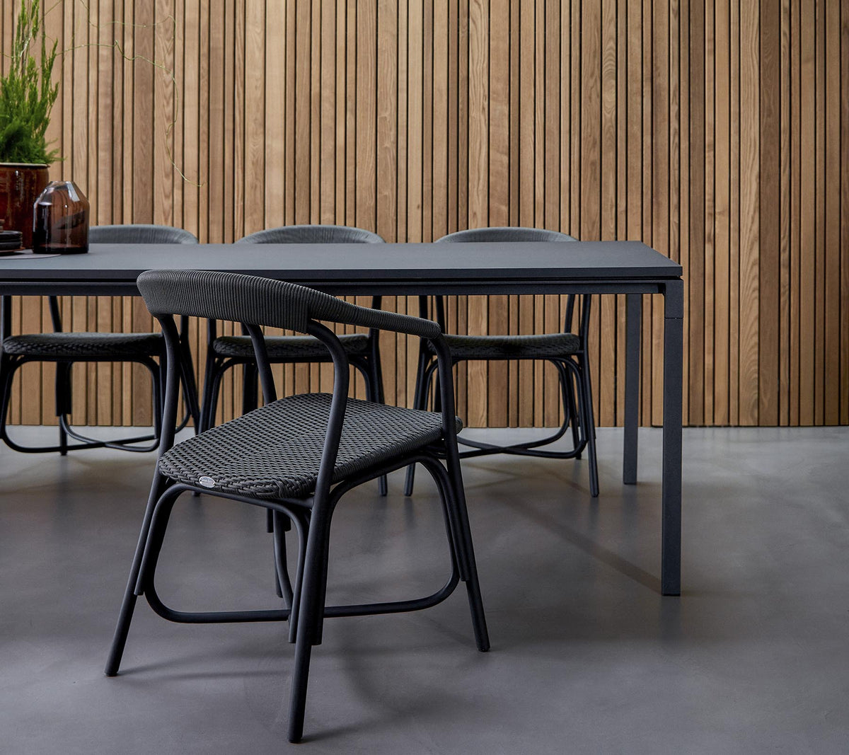 Een moderne eetruimte met een strak tafel omringd door stijlvolle stoelen, tegen een gestructureerde houten achtergrond.