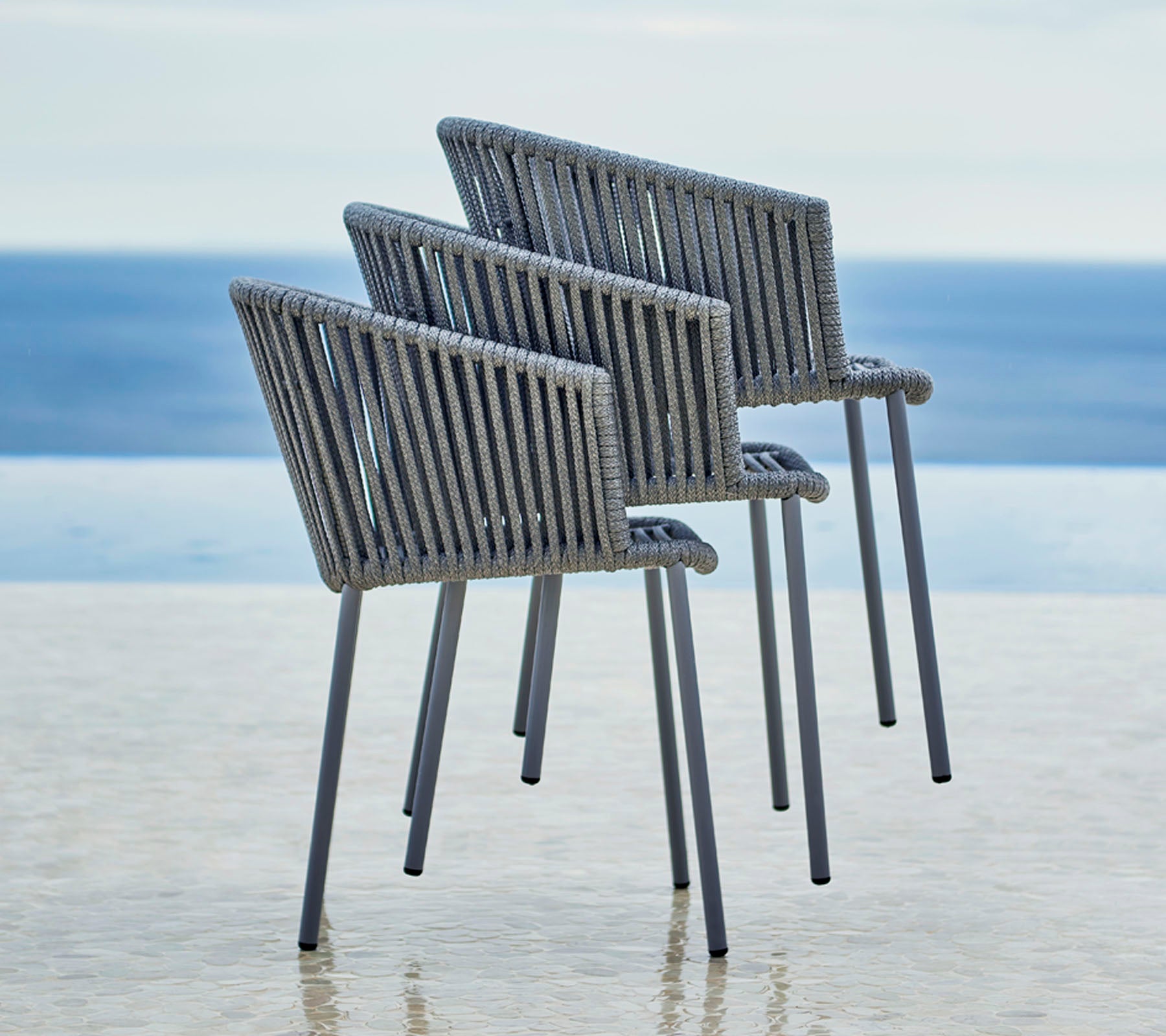 Drie moderne stoelen met een stijlvol ontwerp, met een lattenrugleuning en armleuningen, geplaatst naast een serene wateruitzicht.