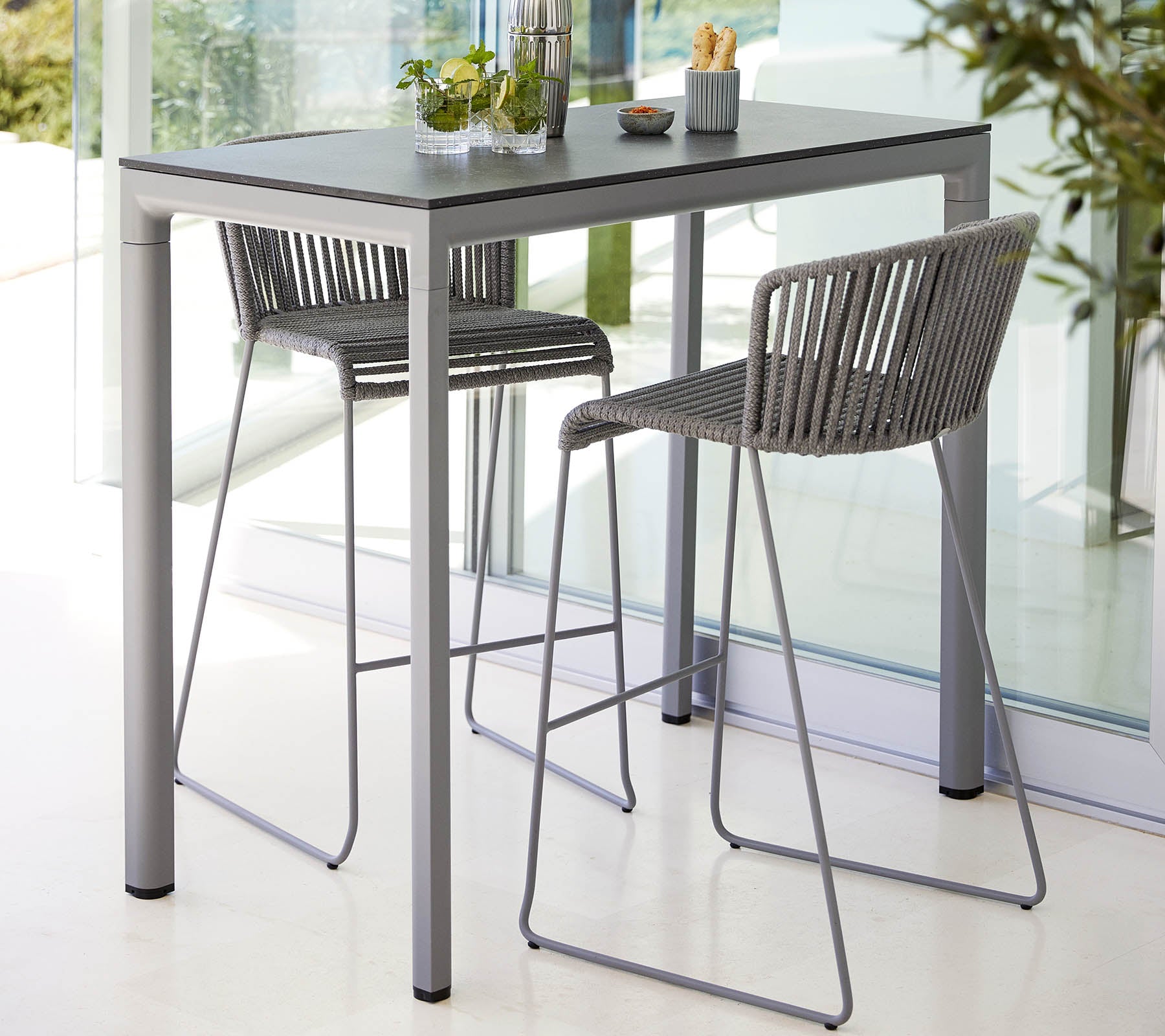 Een moderne tafel met een gladde bovenkant, vergezeld door twee stijlvolle, hoge stoelen, ideaal voor casual dineren of samenkomsten.