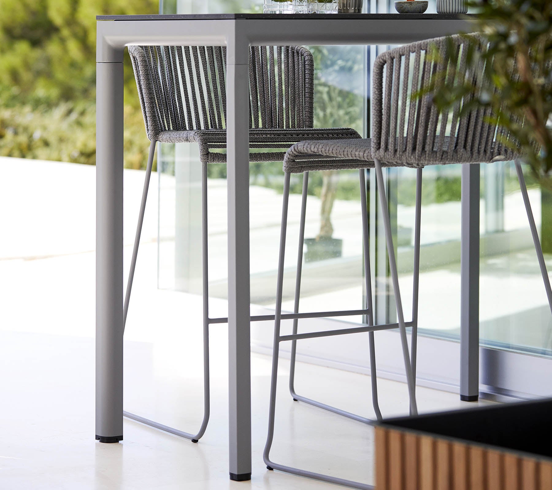 Een slank, modern tafel met bijpassende hoge stoelen met een minimalistisch ontwerp en een stijlvolle metalen frame, aangevuld met natuurlijke groenvoorzieningen.