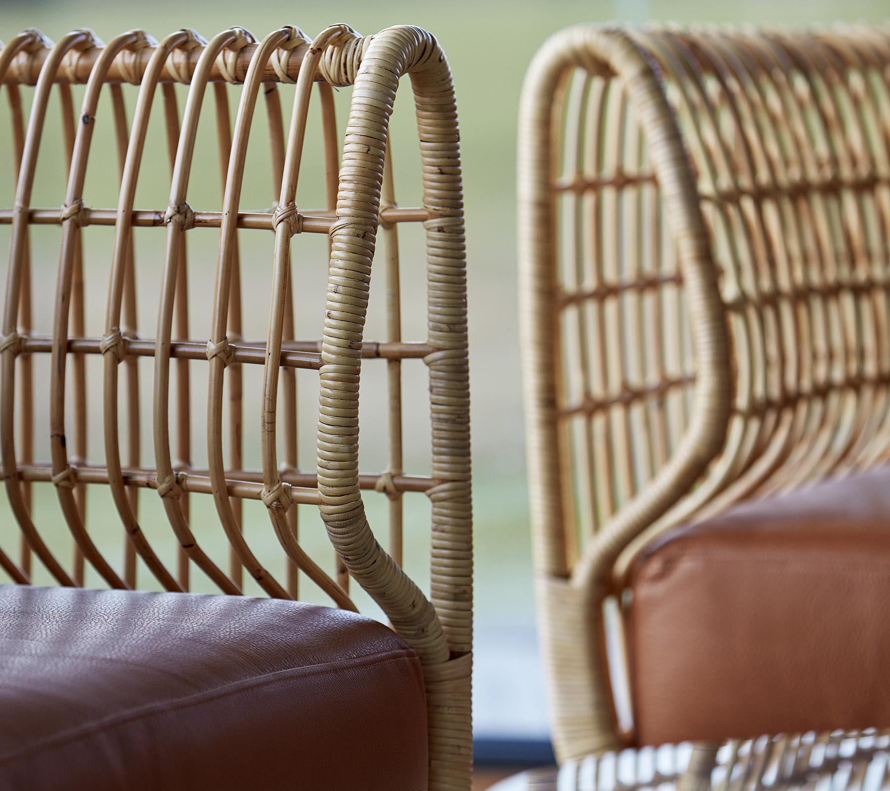 Twee stijlvolle stoelen met gevlochten rieten ruggen en gladde lederen zittingen, die een moderne designtæstiek tonen.