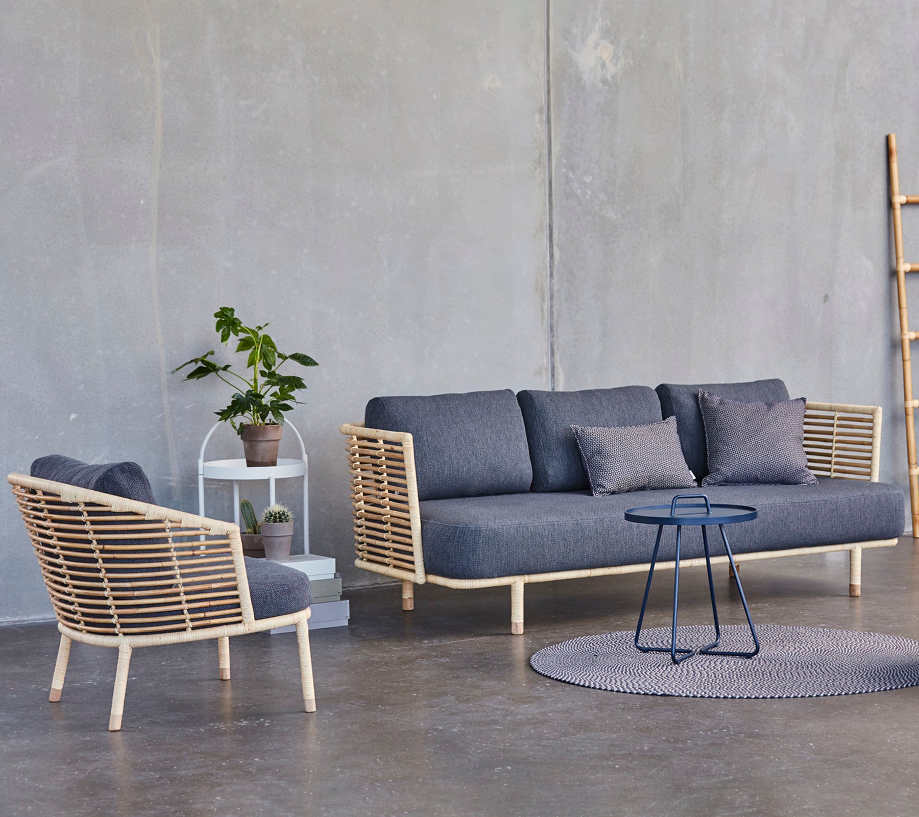 Een moderne zitopstelling met een stijlvolle bank en fauteuil met houten accenten, vergezeld van een klein bijzettafel en een potplant.