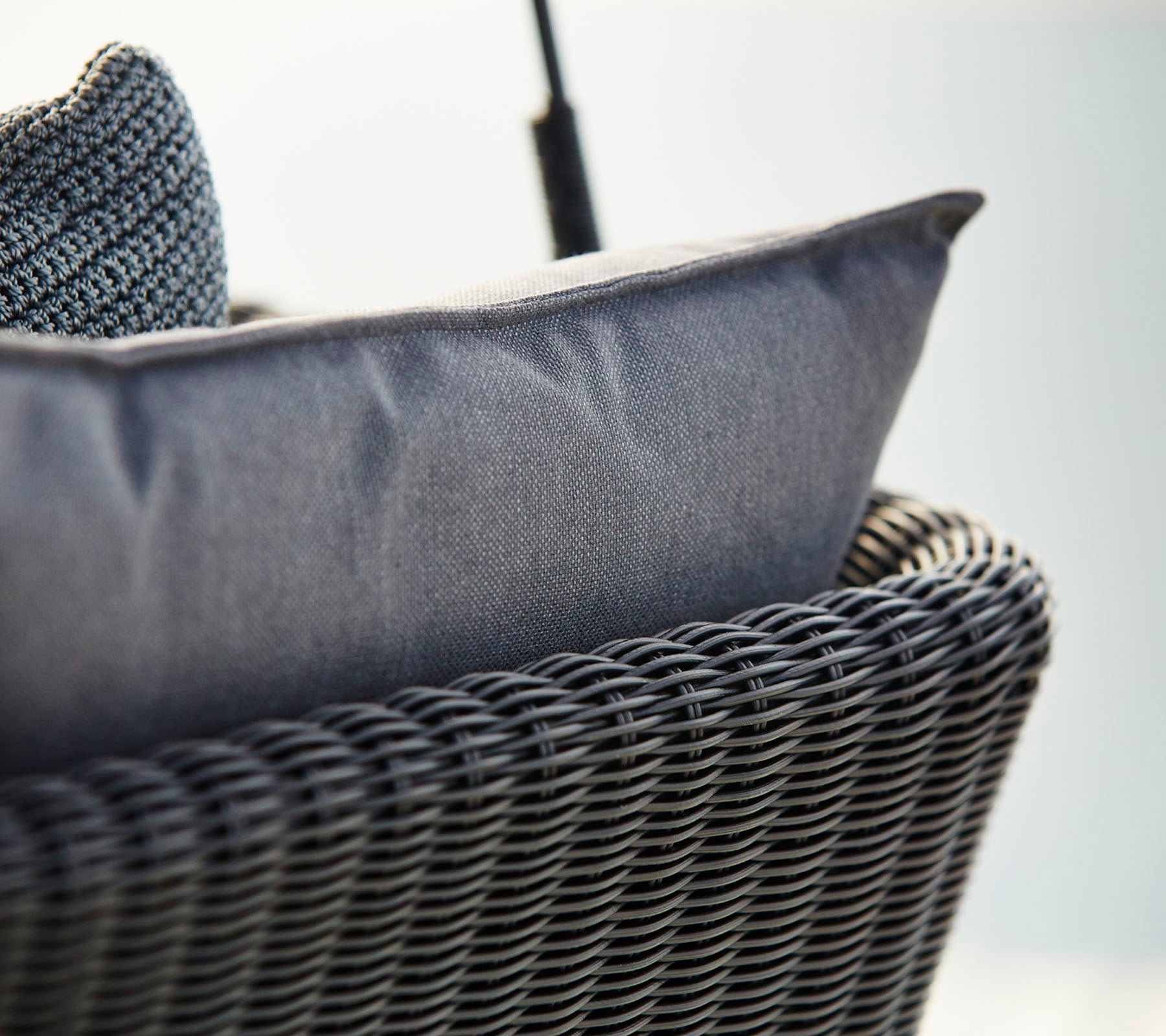 Close-up van een geweven mandstoel met een gestructureerd donkergrijs kussen, dat comfort en modern design benadrukt.