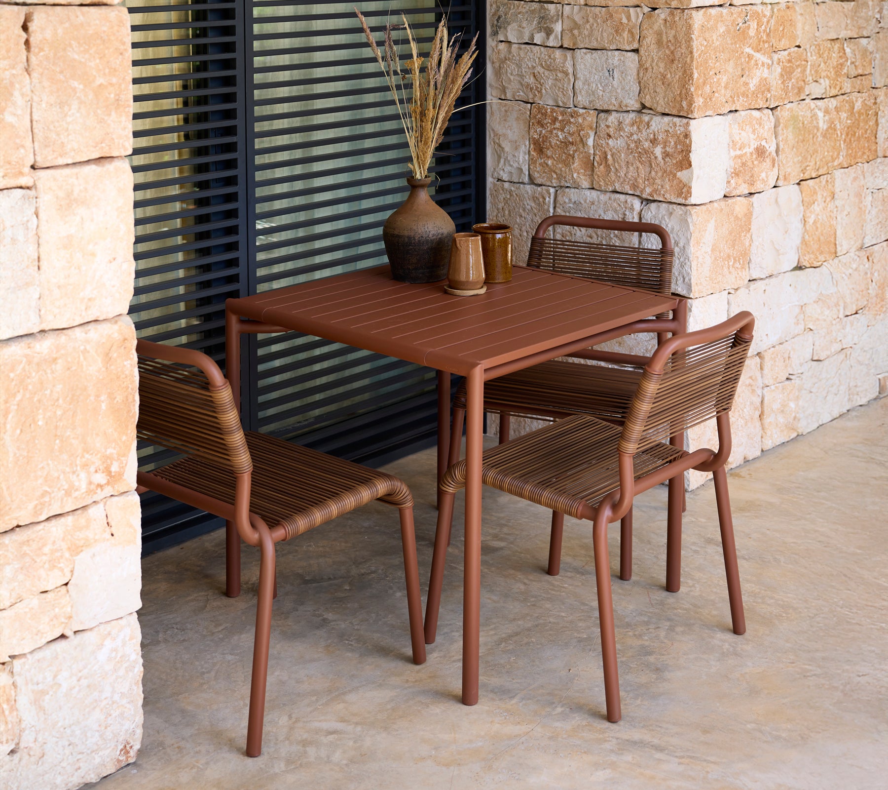 Bruine tafel en stoelen in een moderne buitenomgeving met stenen muren.