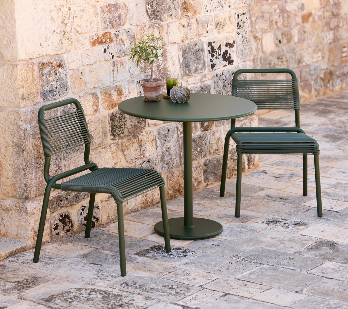 Twee groene stoelen en een ronde groene tafel in een buitenomgeving.