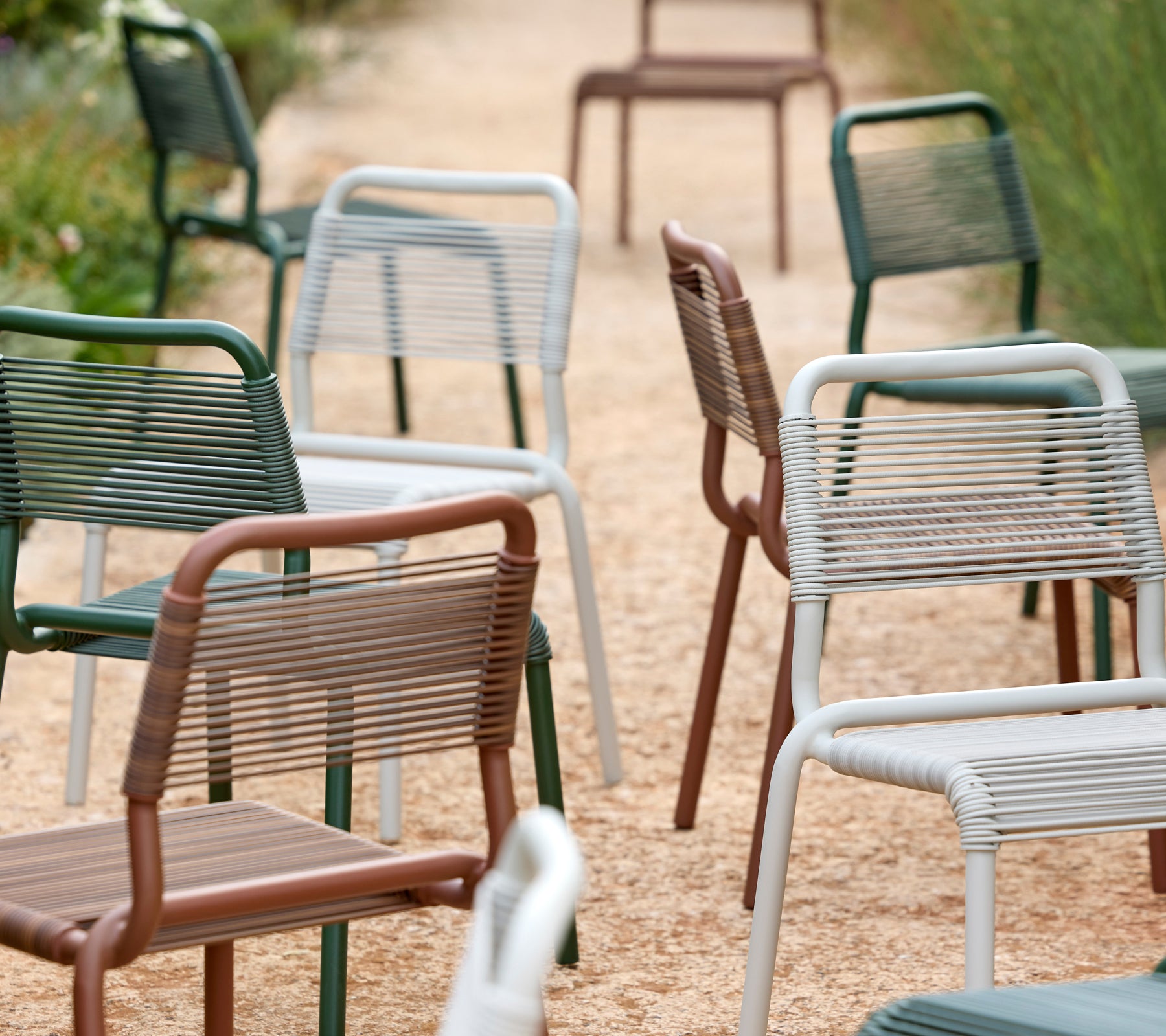 Een reeks moderne stoelen in groen, grijs, bruin en wit op een grindpad.