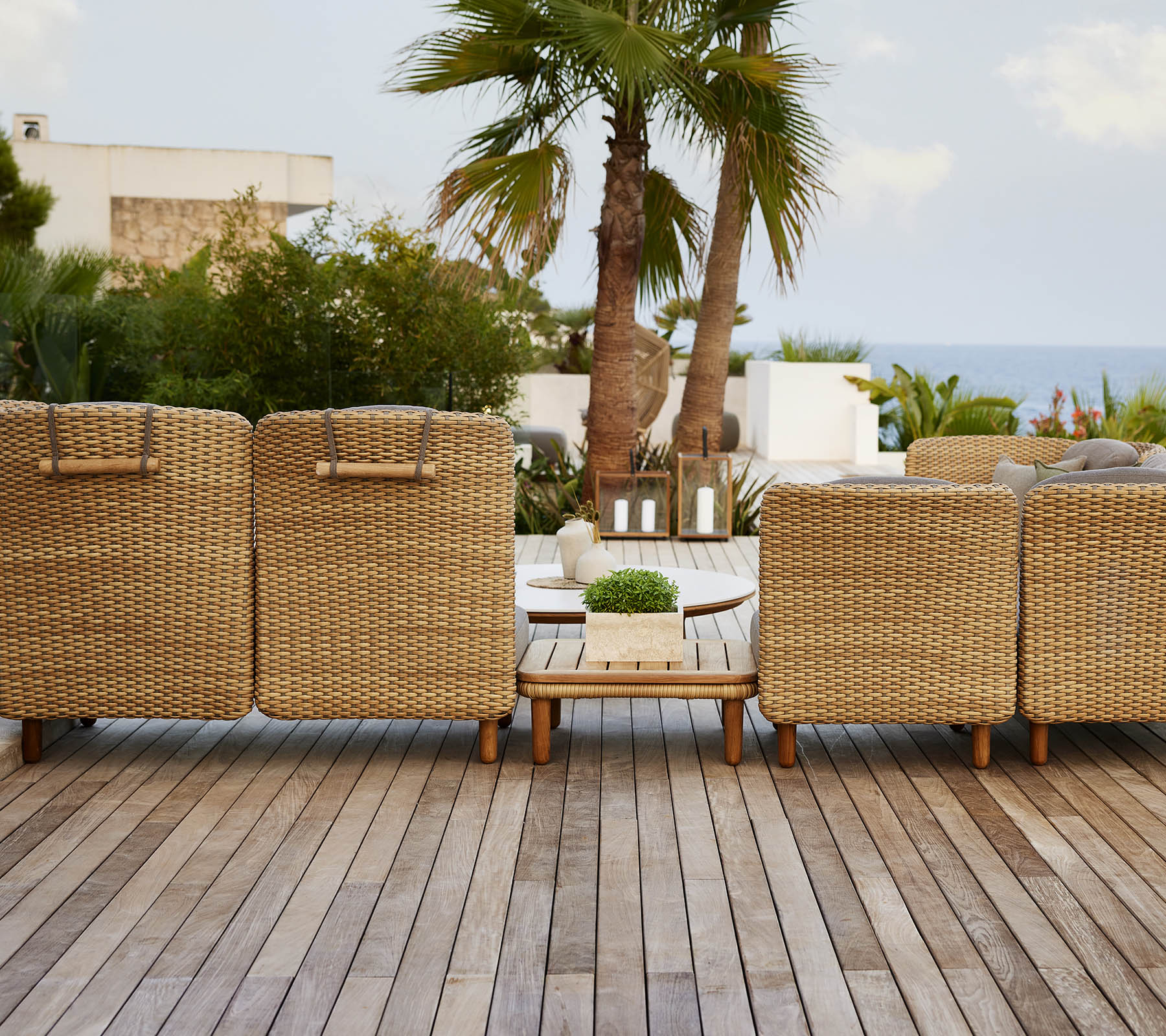 Een rij geweven loungestoelen met uitzicht op een schilderachtig panorama, met een houten terras en tropische planten op de achtergrond.