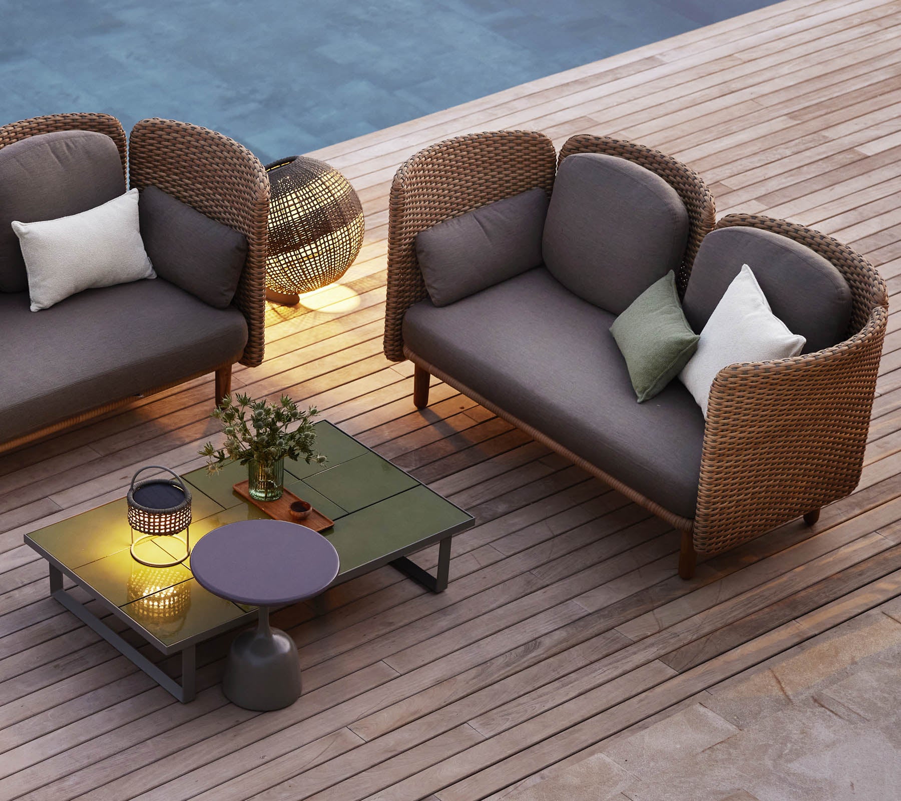 Een gezellige zithoek met twee gebogen loungesofa's, een laag tafeltje, decoratieve kussens en sfeerverlichting.