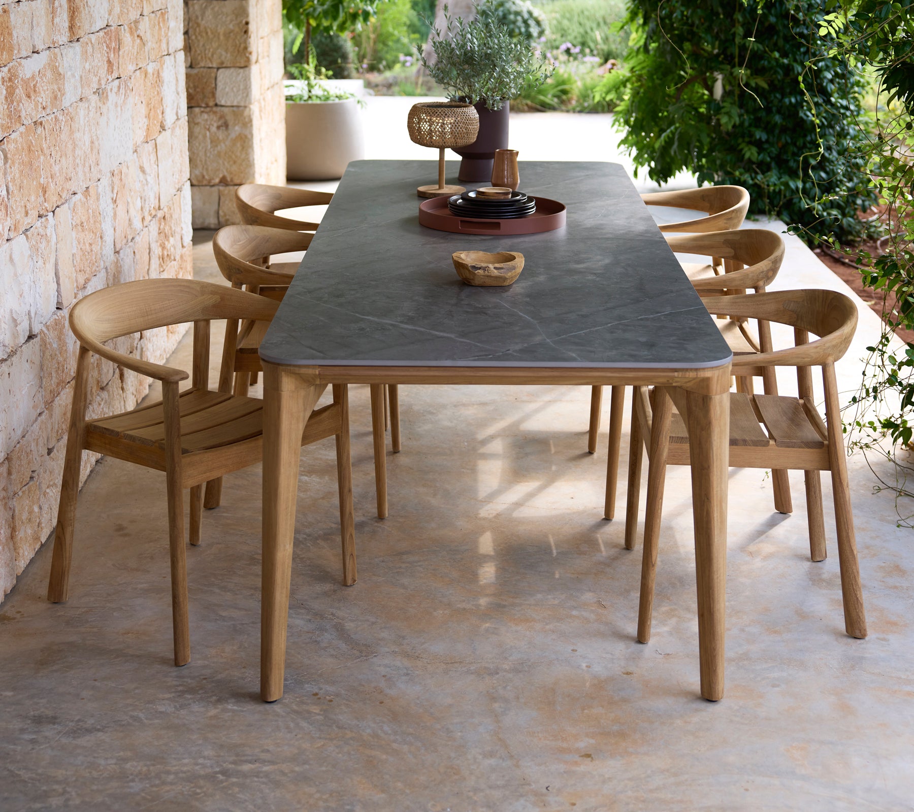 Moderne buitentafel met zwarte oppervlakte en houten stoelen in een natuurlijke omgeving.