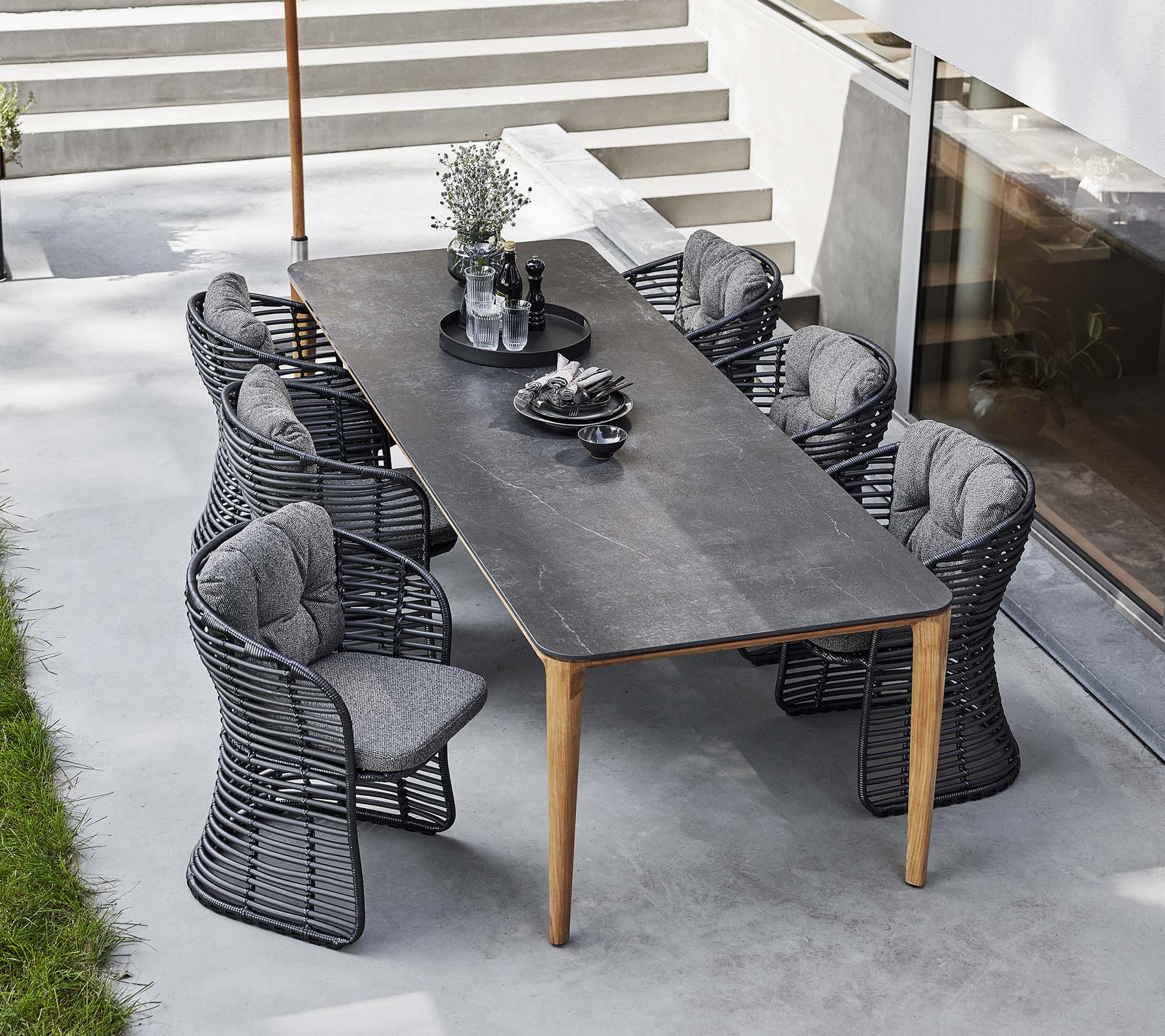 Wicker stoelen omringen een strak tafel, aangevuld met een klassieke parasol en decoratieve middelpunt voor een uitnodigende buiten eetopstelling.
